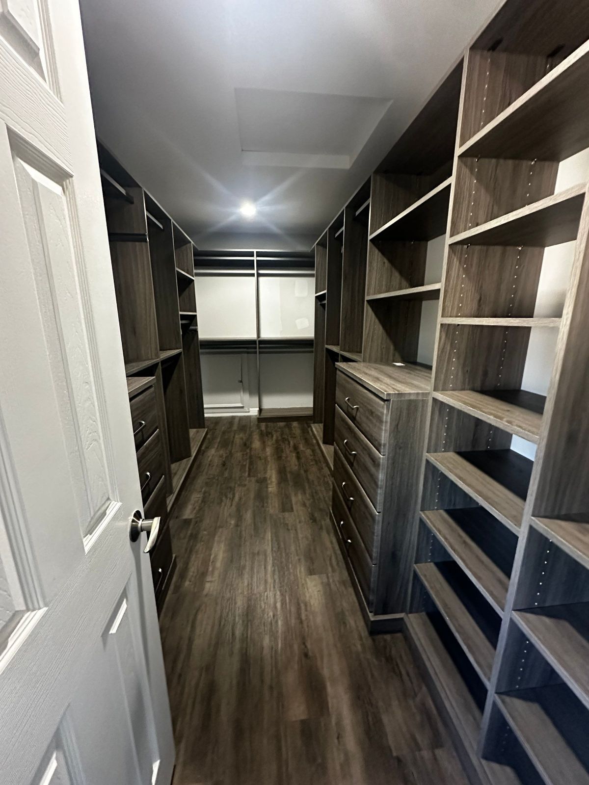 Walk-in closet with dark wood shelving and drawers, a light wood floor, and a mirrored back wall.