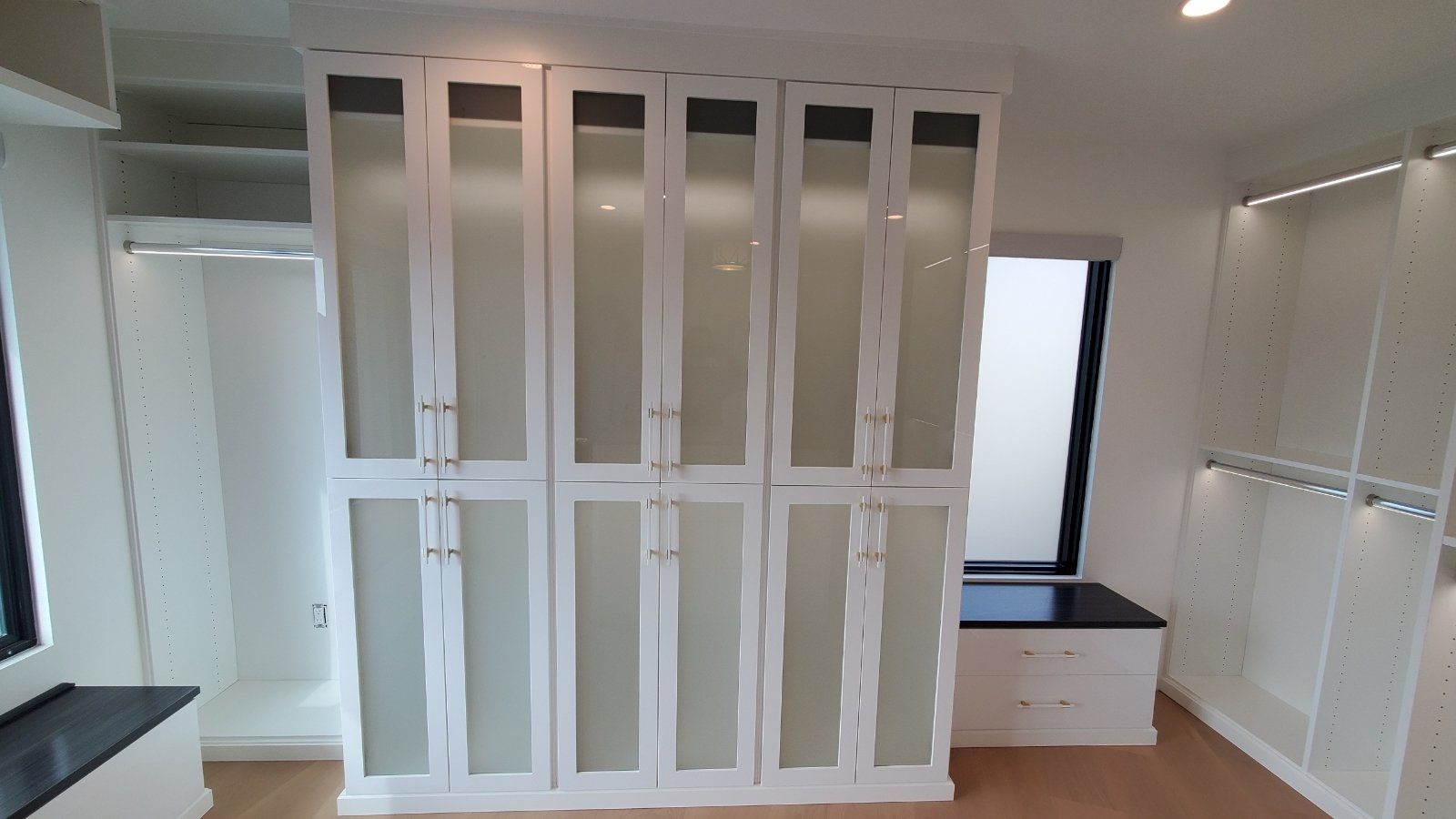 a white finish walk-in closet with glass door cabinet