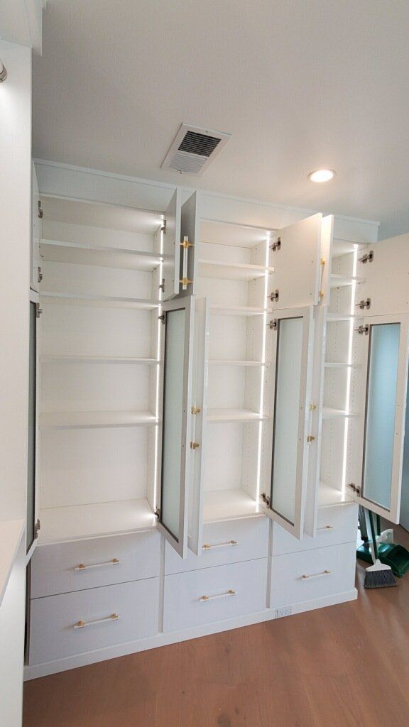 a white finish walk in closet  cabinet with strip lights and  slide out mirror