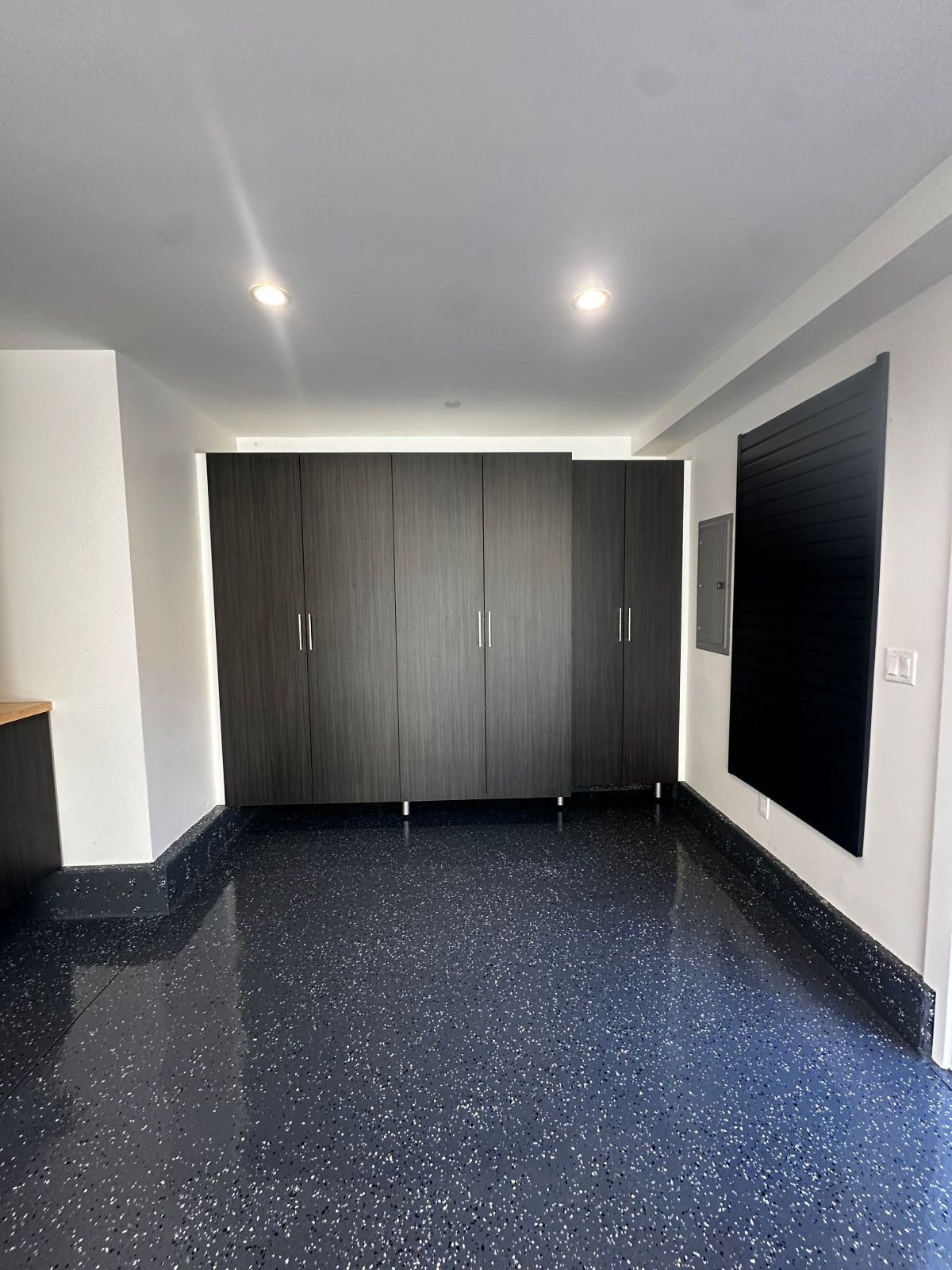 Dark gray storage cabinets in a room with a speckled black and gray floor and white walls.