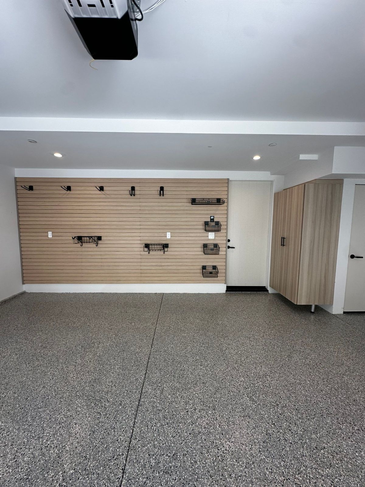 A clean garage with a speckled floor, wood-paneled wall with storage, and cabinets.