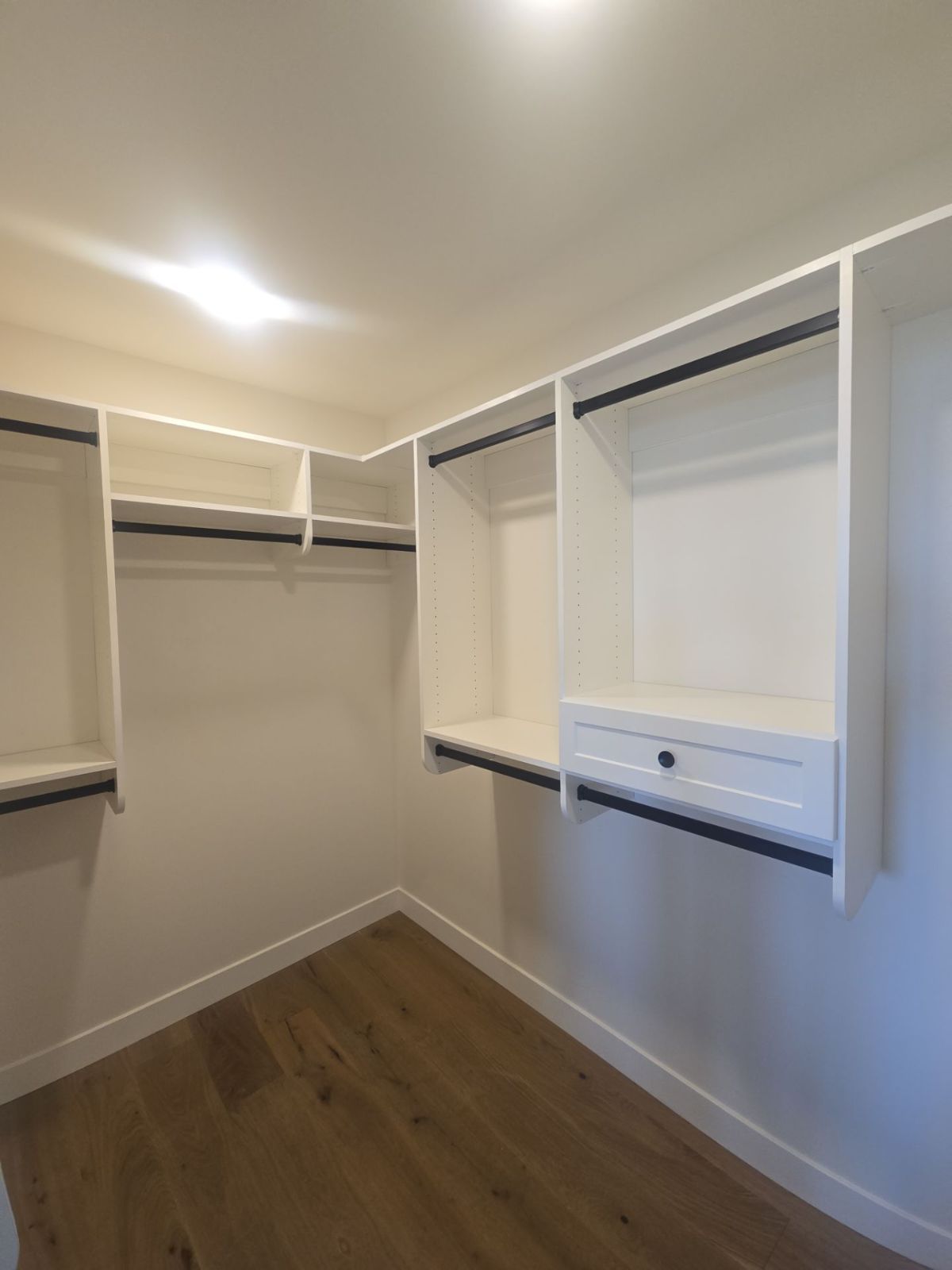 Empty walk-in closet with white shelves, black rods, and wood-look flooring.