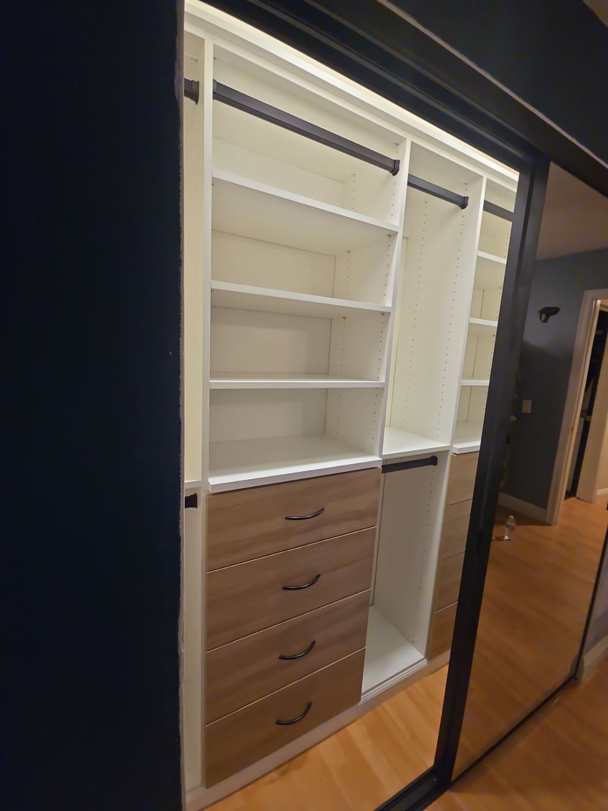 Custom closet with white shelves, drawers, and hanging rods. The doors are mirrored.