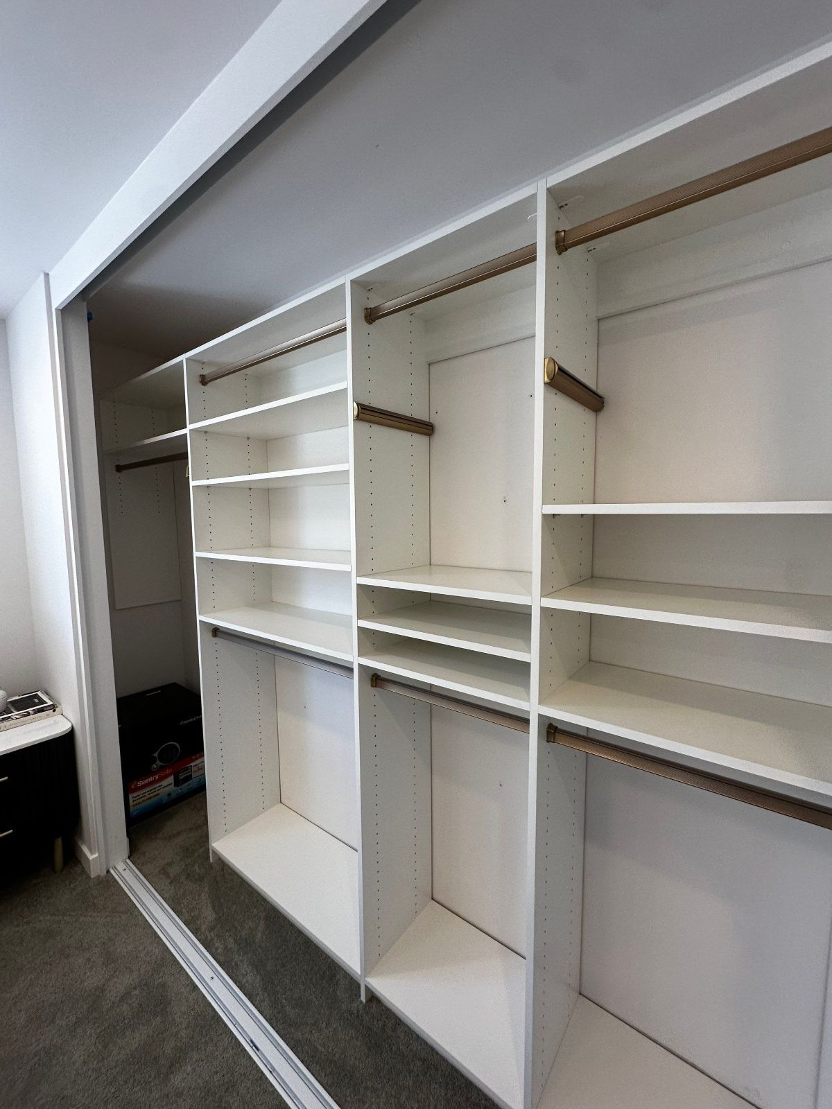 White built-in closet with shelves and hanging rods. Gray carpeted floor. Sliding door on the left.