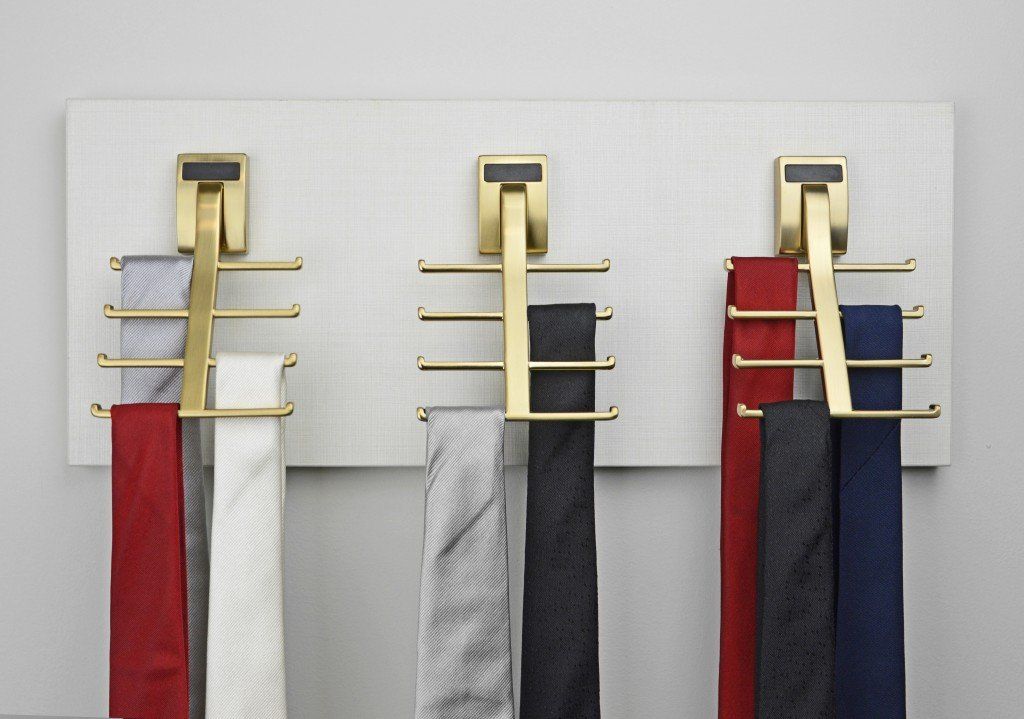 Three wall hooks holding striped scarves and a red, black, and blue scarf on a white wall