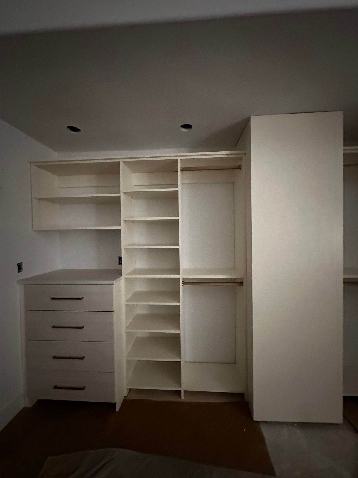White custom-built closet with drawers, shelves, and hanging rods. Interior view, neutral tones.