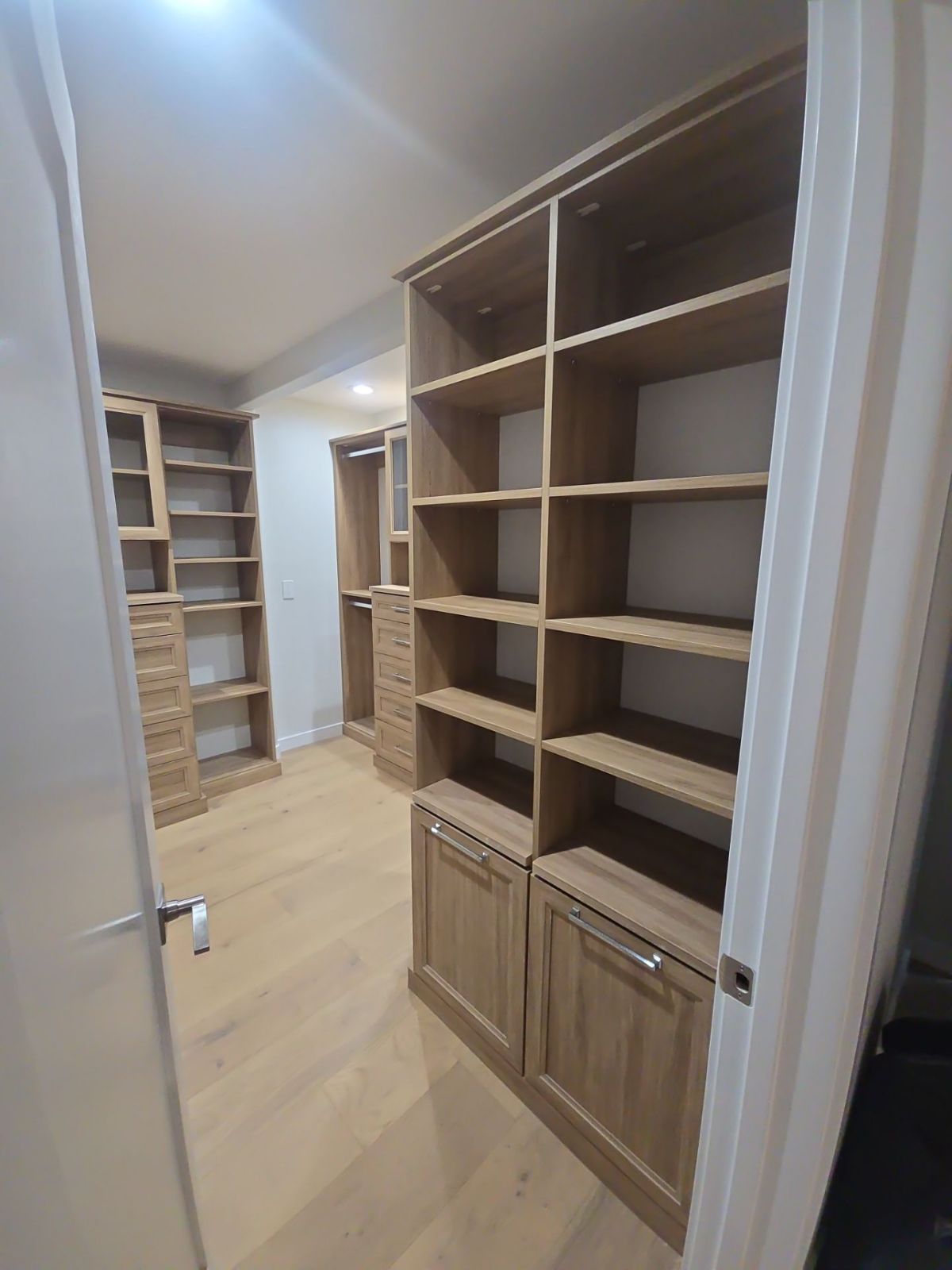 Walk-in closet with light wood shelving and cabinets; open door frame in foreground.