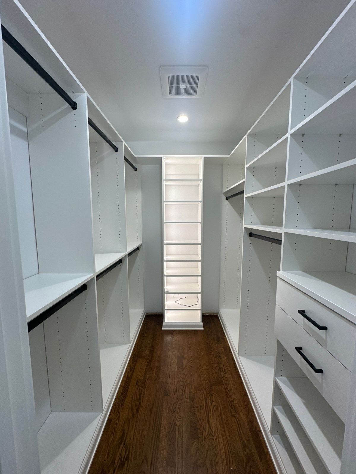 White walk-in closet with shelves, hanging rods, and dark wood flooring.