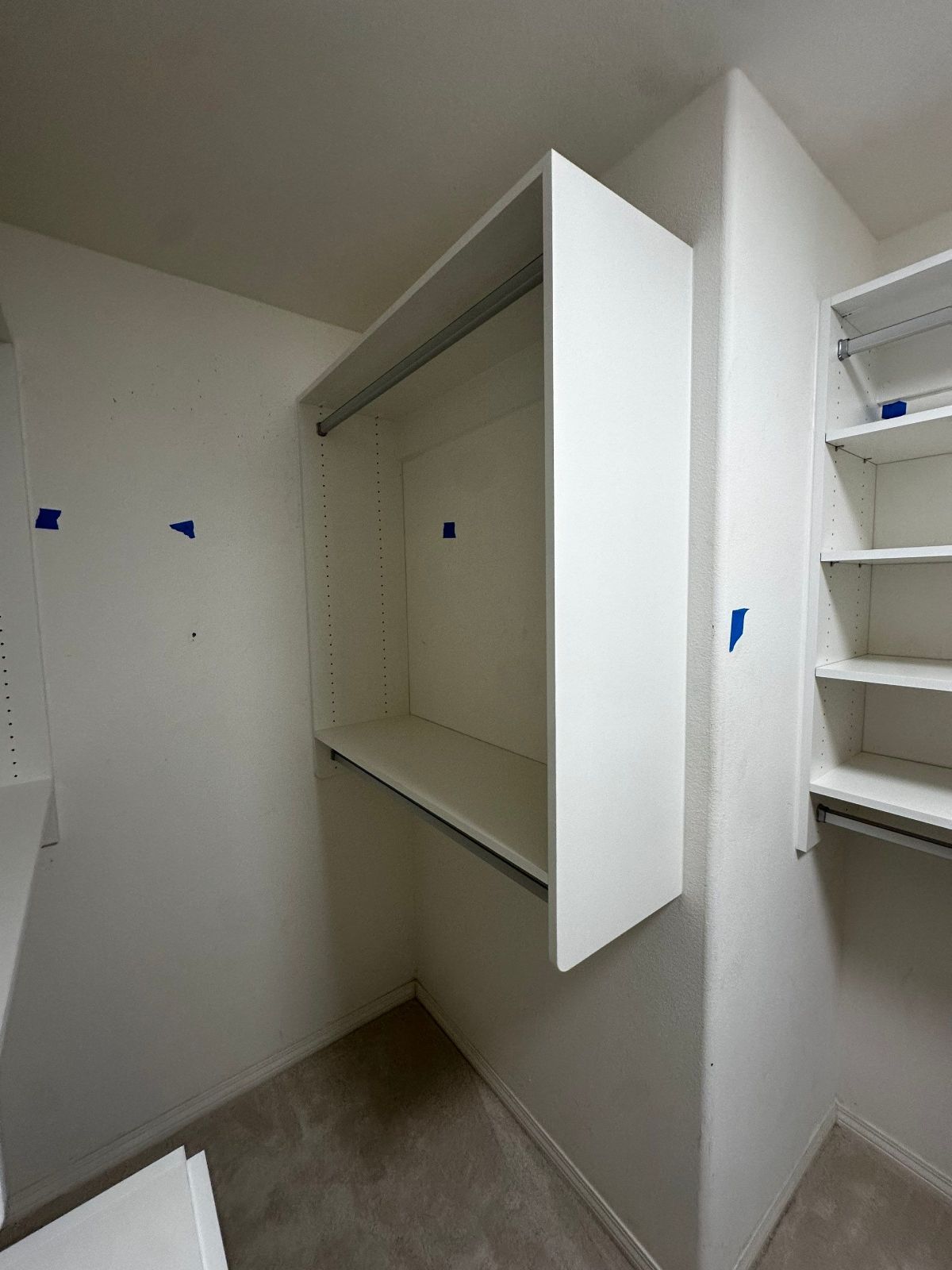 White closet with built-in shelves and hanging rods. Small room with carpeted floor.