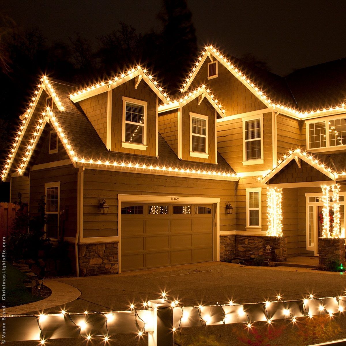 House decorated with colorful Christmas lights at night; lawn lined with illuminated star shapes.