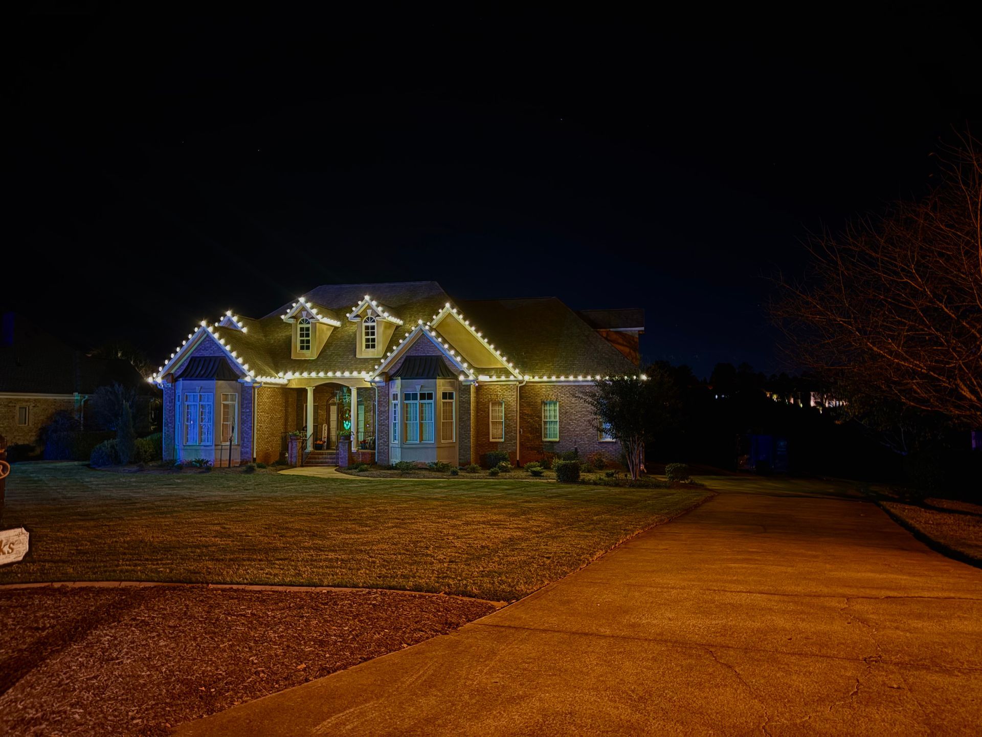House at night, illuminated with white Christmas lights along the roof and windows.