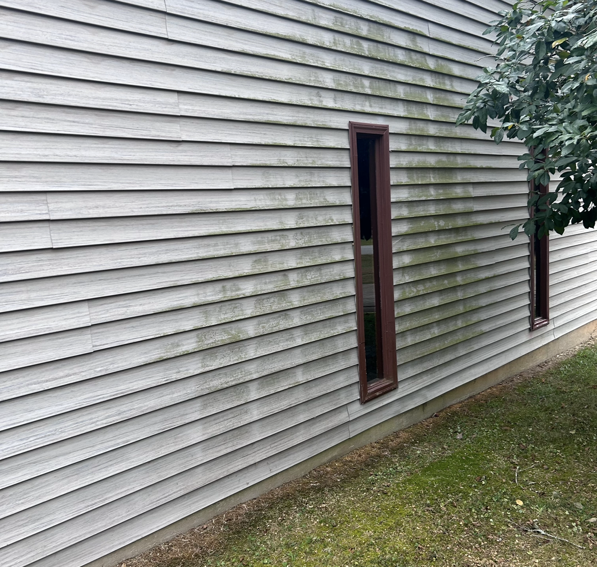 A man in a hat is cleaning a sidewalk with a hose.