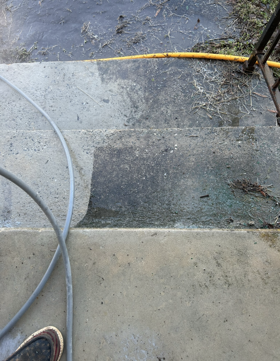 A man in a yellow jacket is using a high pressure washer to clean the sidewalk.