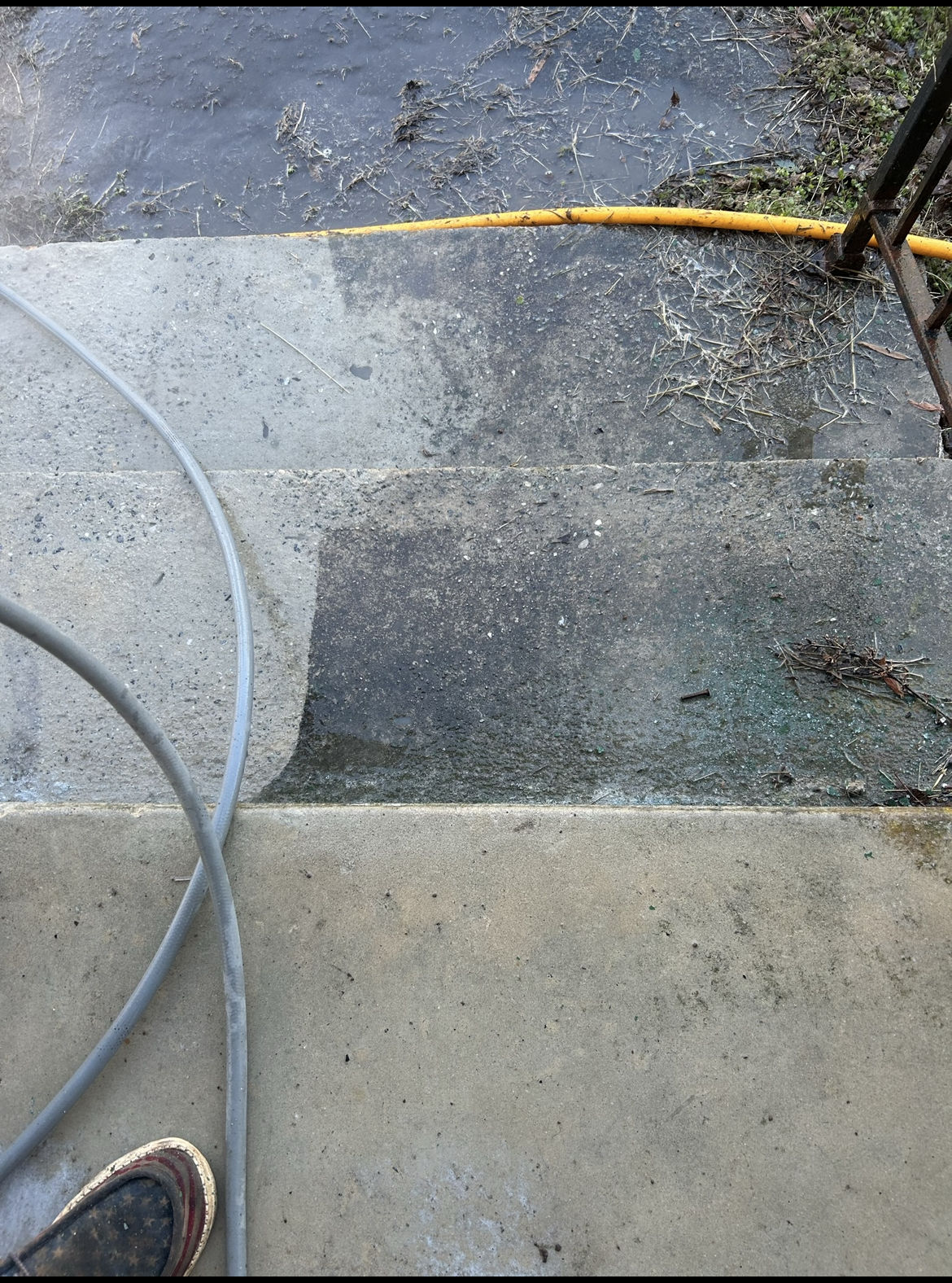 A person is cleaning a concrete sidewalk with a hose.