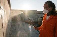 A man wearing a mask is spraying a wall with a hose.