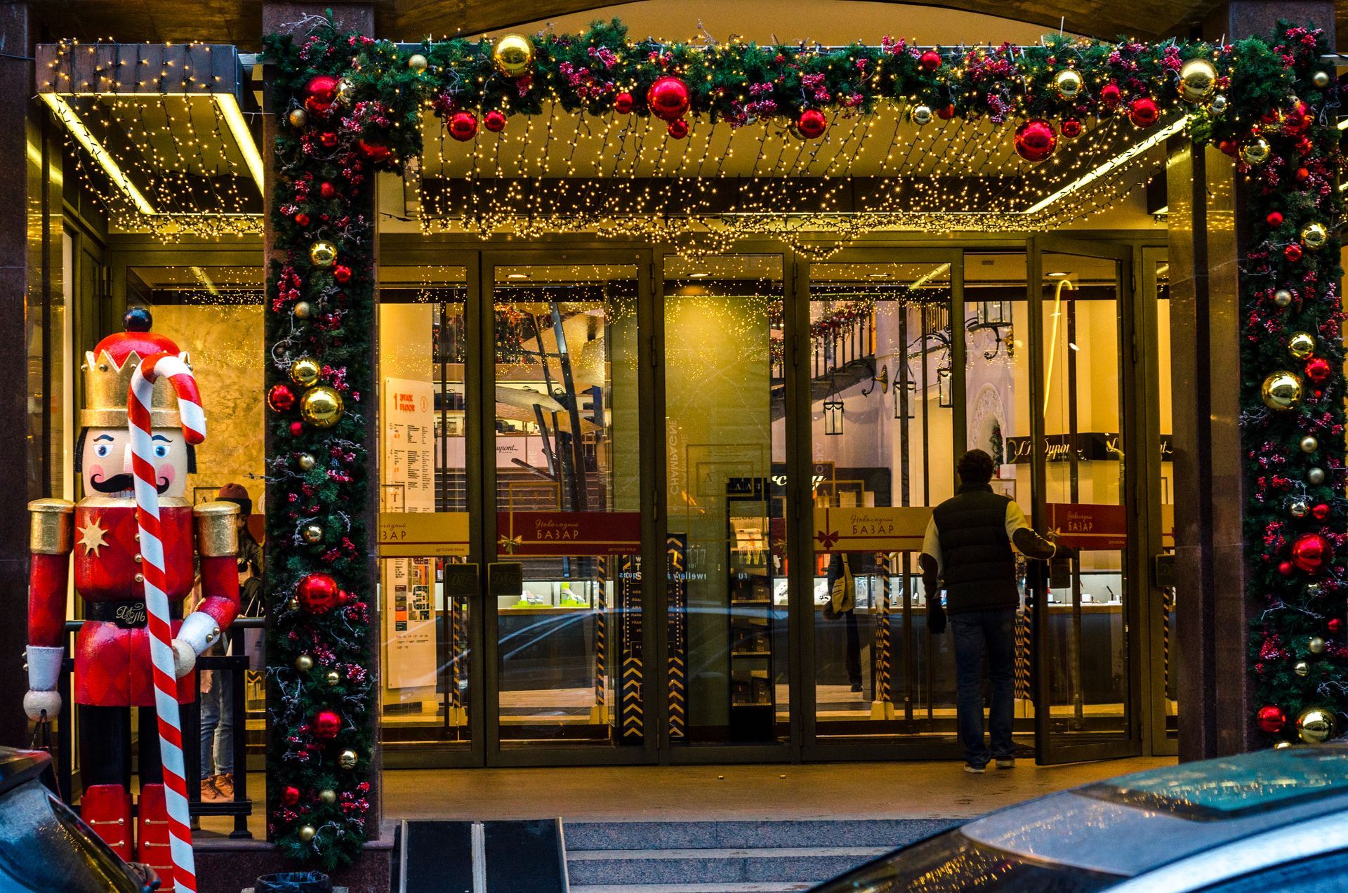 Store entrance with Christmas decorations and a nutcracker statue. A person enters.