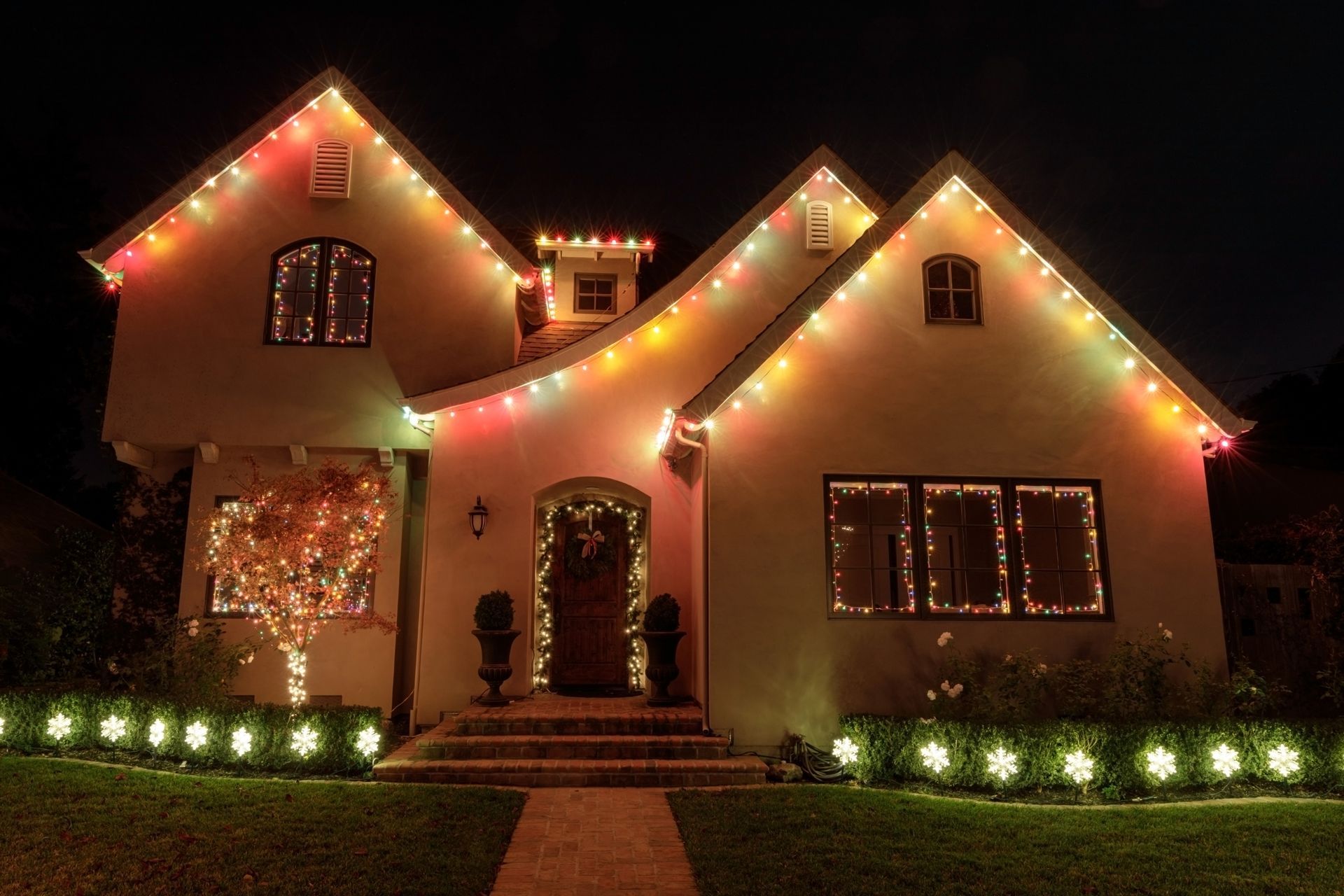 House decorated with colorful Christmas lights at night; lawn lined with illuminated star shapes.