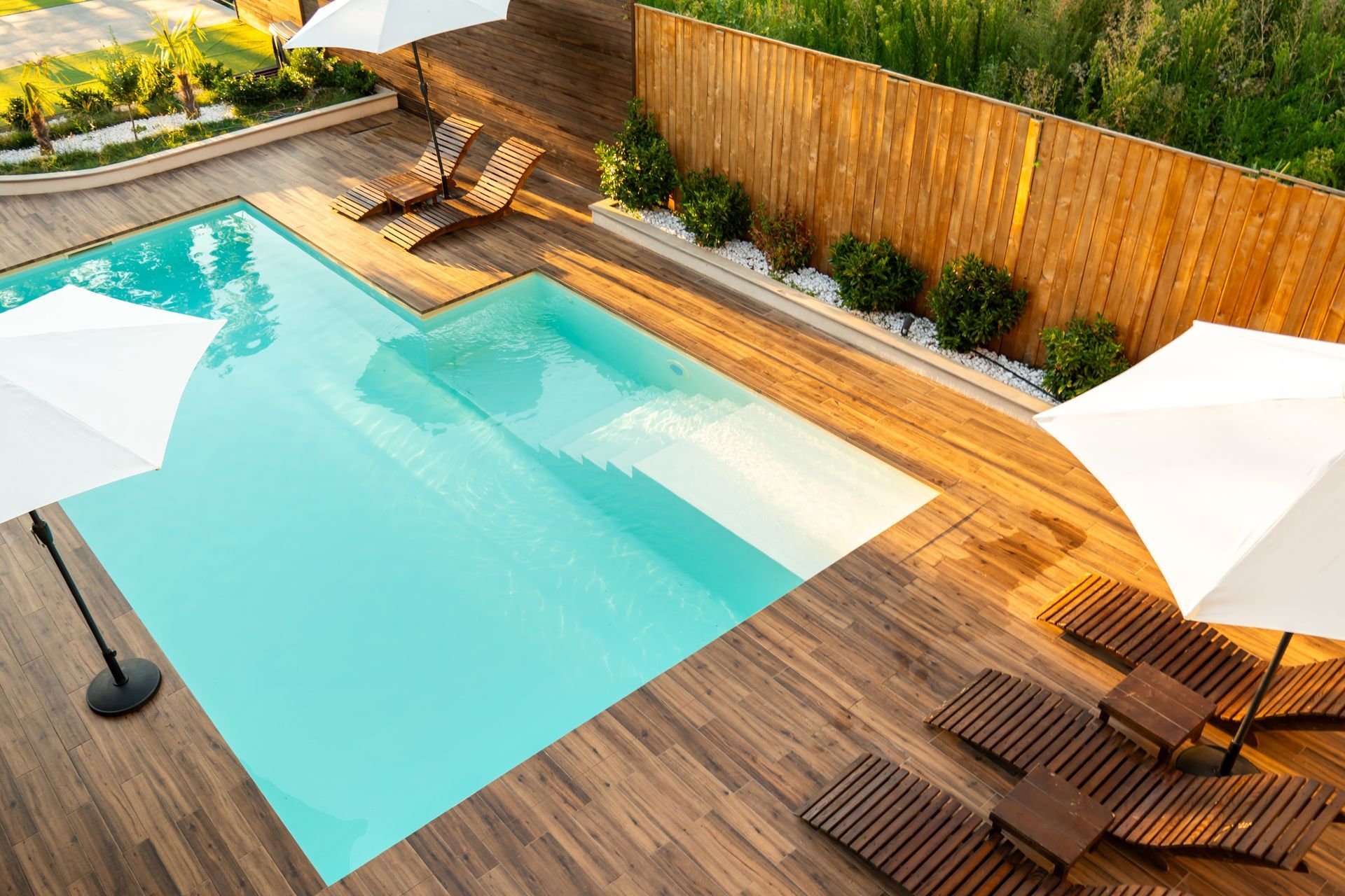 Pool with wooden deck, lounge chairs, and white umbrellas; a bamboo fence surrounds the pool.