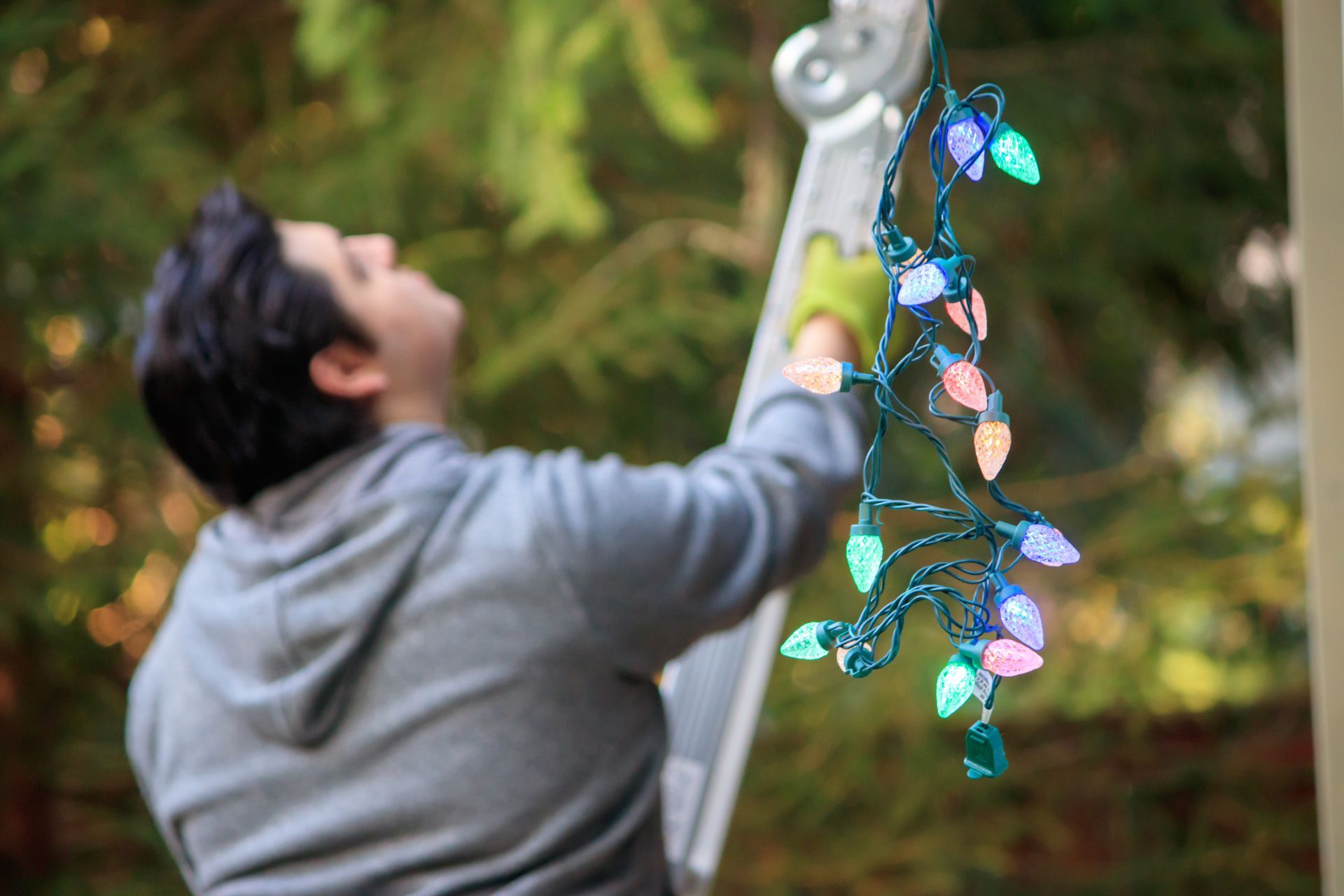 Person on ladder hanging colorful Christmas lights outdoors.
