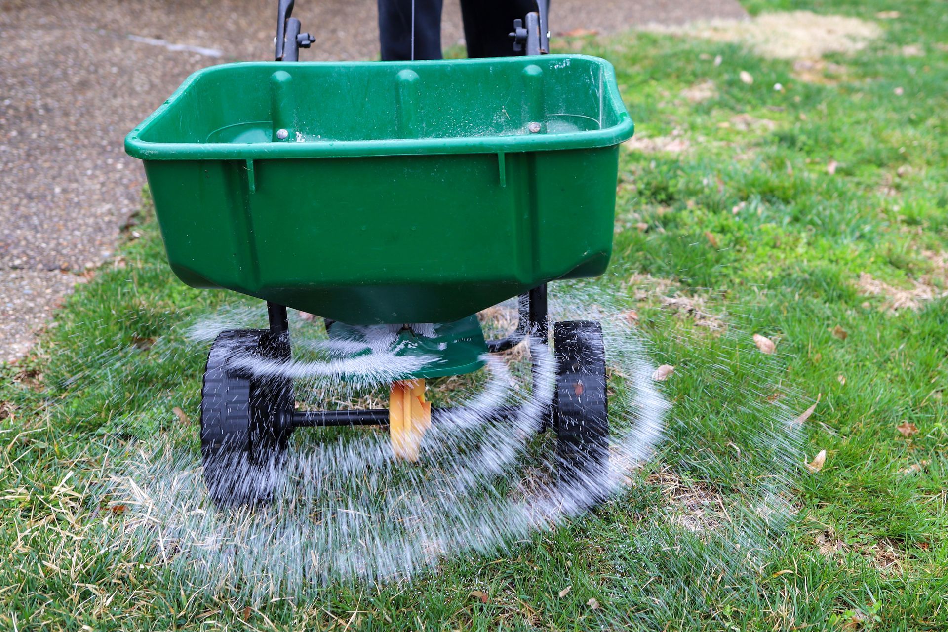 A lawncare professional uses a distributor to spread fertilizer on a customer's lawn.