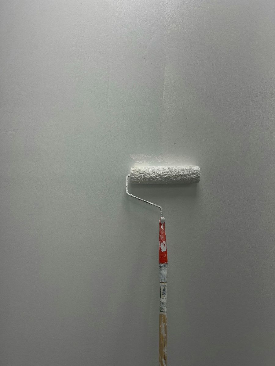 Paint roller on a gray wall, mid-painting with a white strip near the top