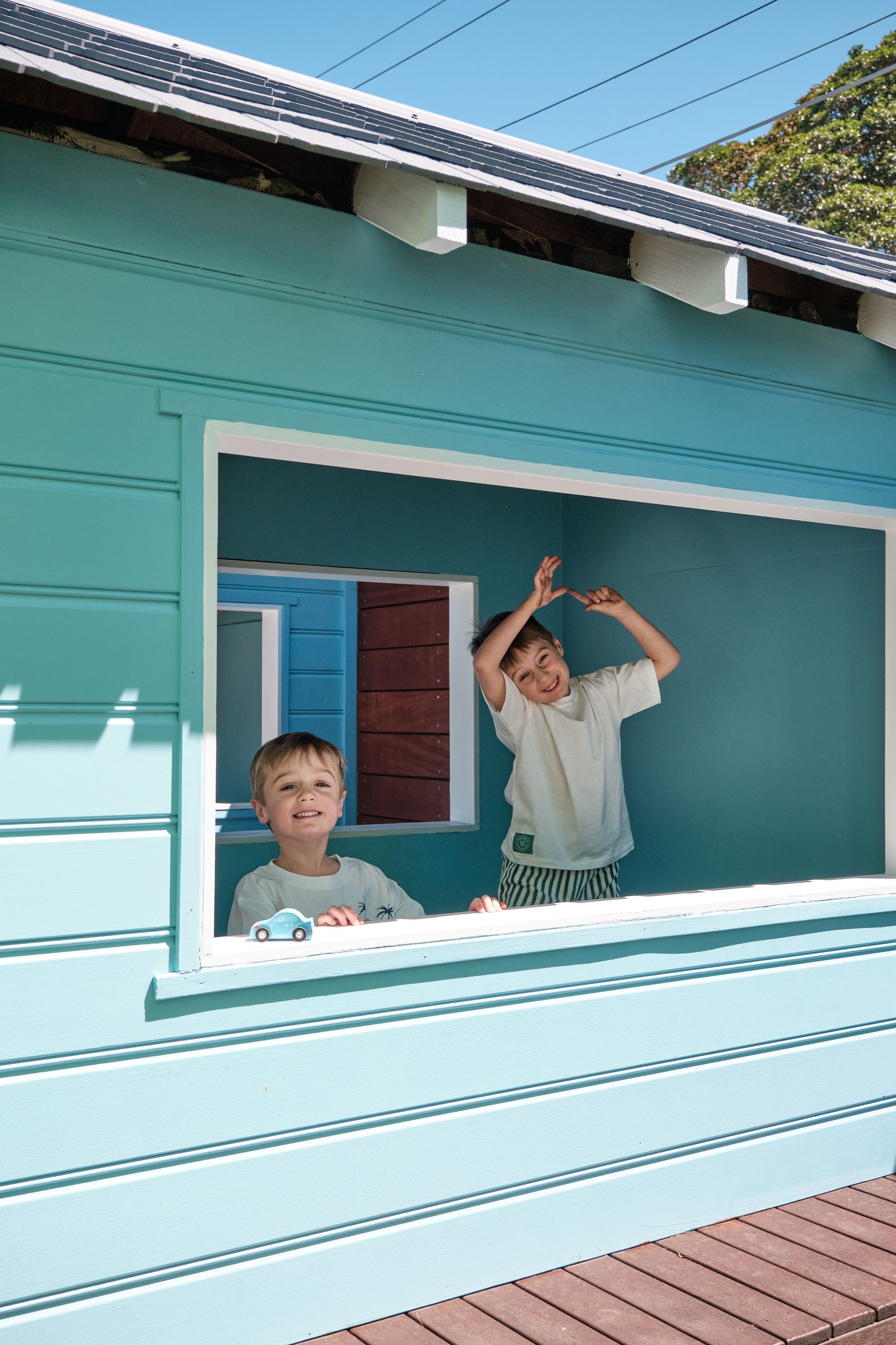 Two children inside a blue playhouse. One smiles, the other makes a funny face.
