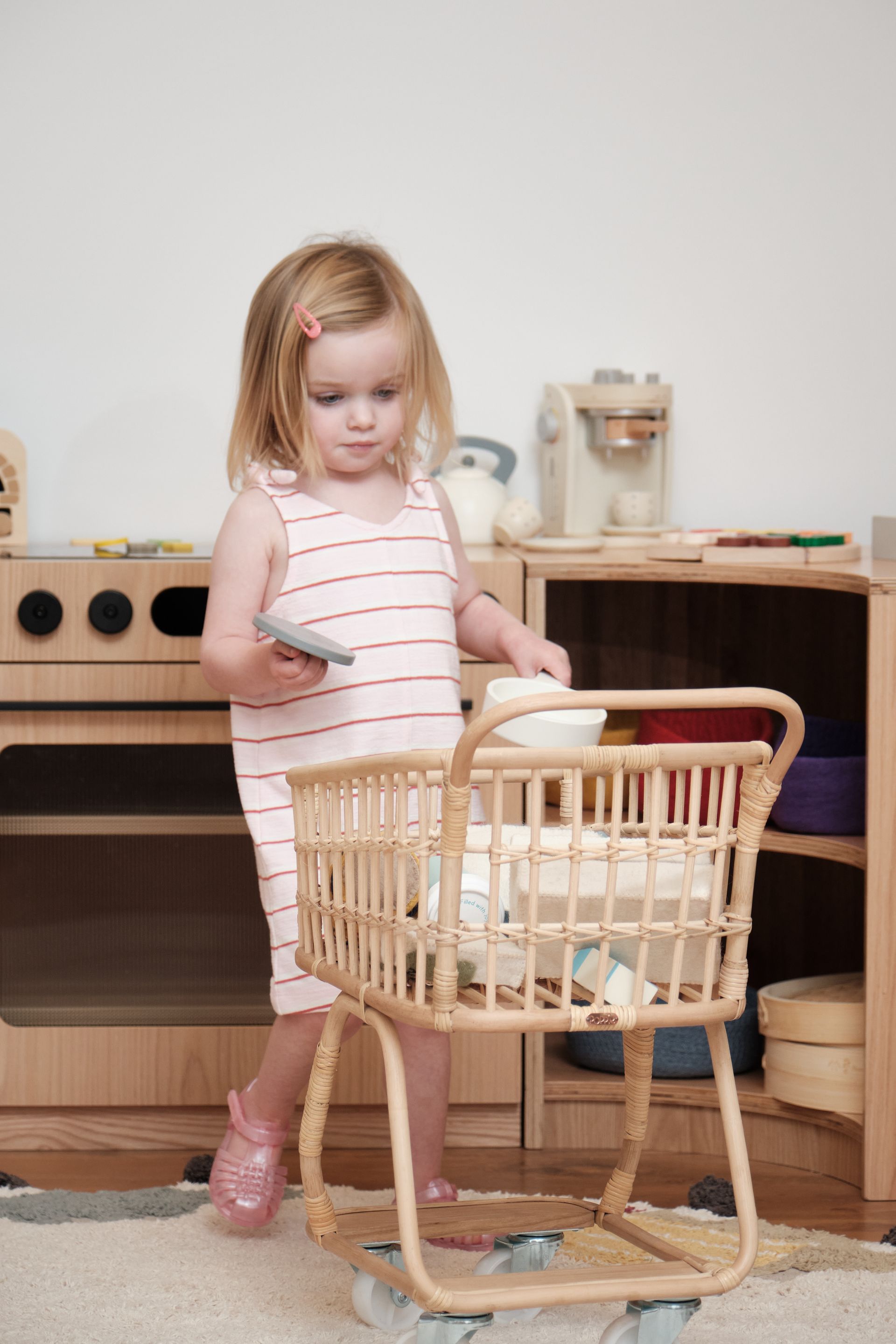 Child playing with a toy shopping cart in a light-colored playroom.