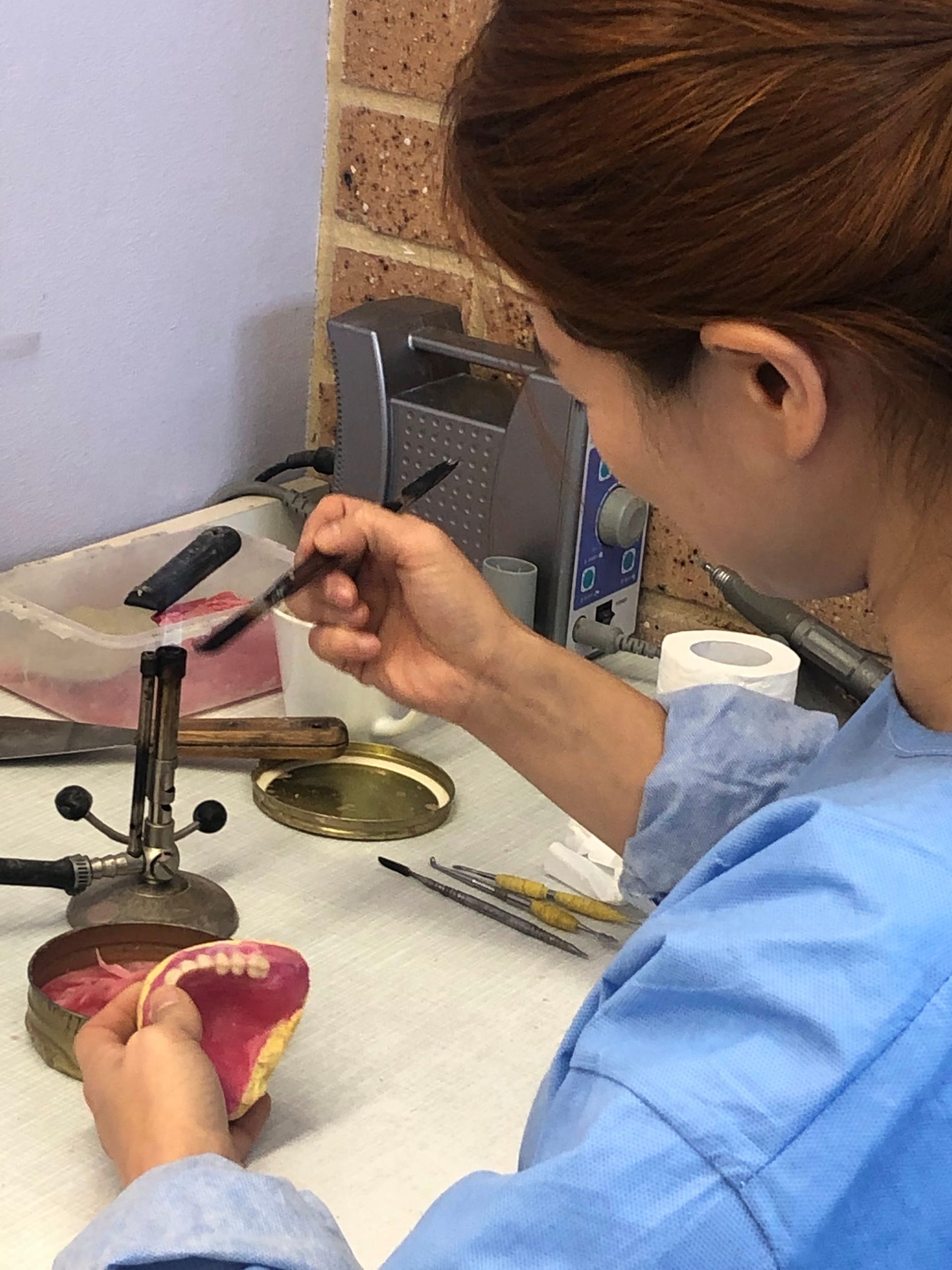 Dental Technician Working on a Set of Dentures With a Brush — My Denture Clinic in Armidale, NSW