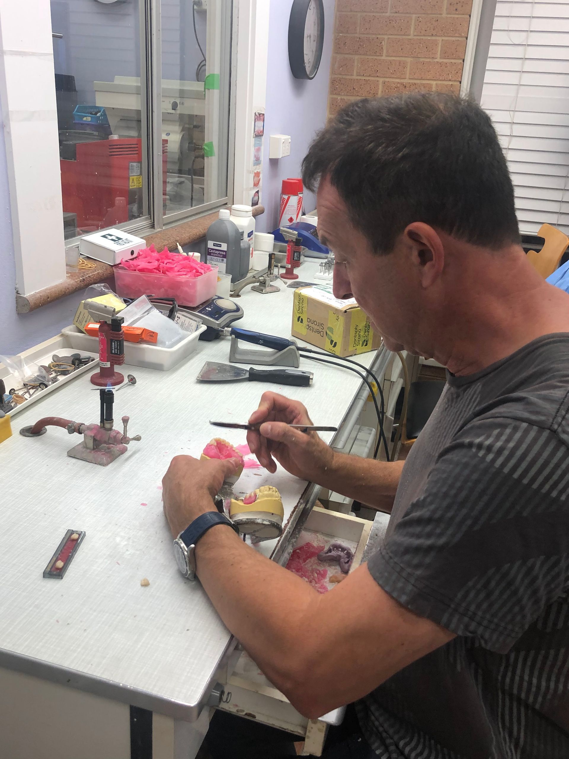 Man Painting a Dental Mold at a Workbench — My Denture Clinic in Benowa, QLD