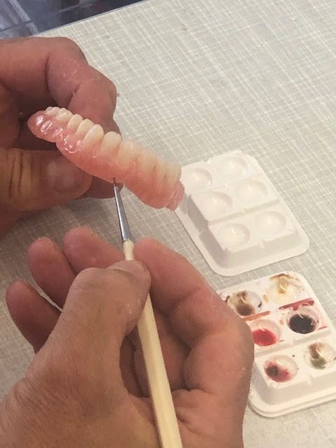 Person Painting a Row of Artificial Teeth With a Small Brush — My Denture Clinic in Armidale, NSW