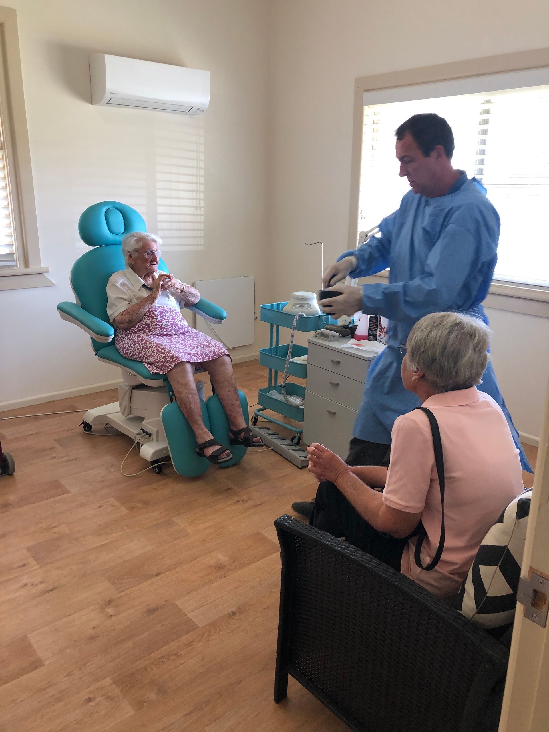 Dentist in Blue Scrubs Prepares While an Elderly Woman — My Denture Clinic in Benowa, QLD