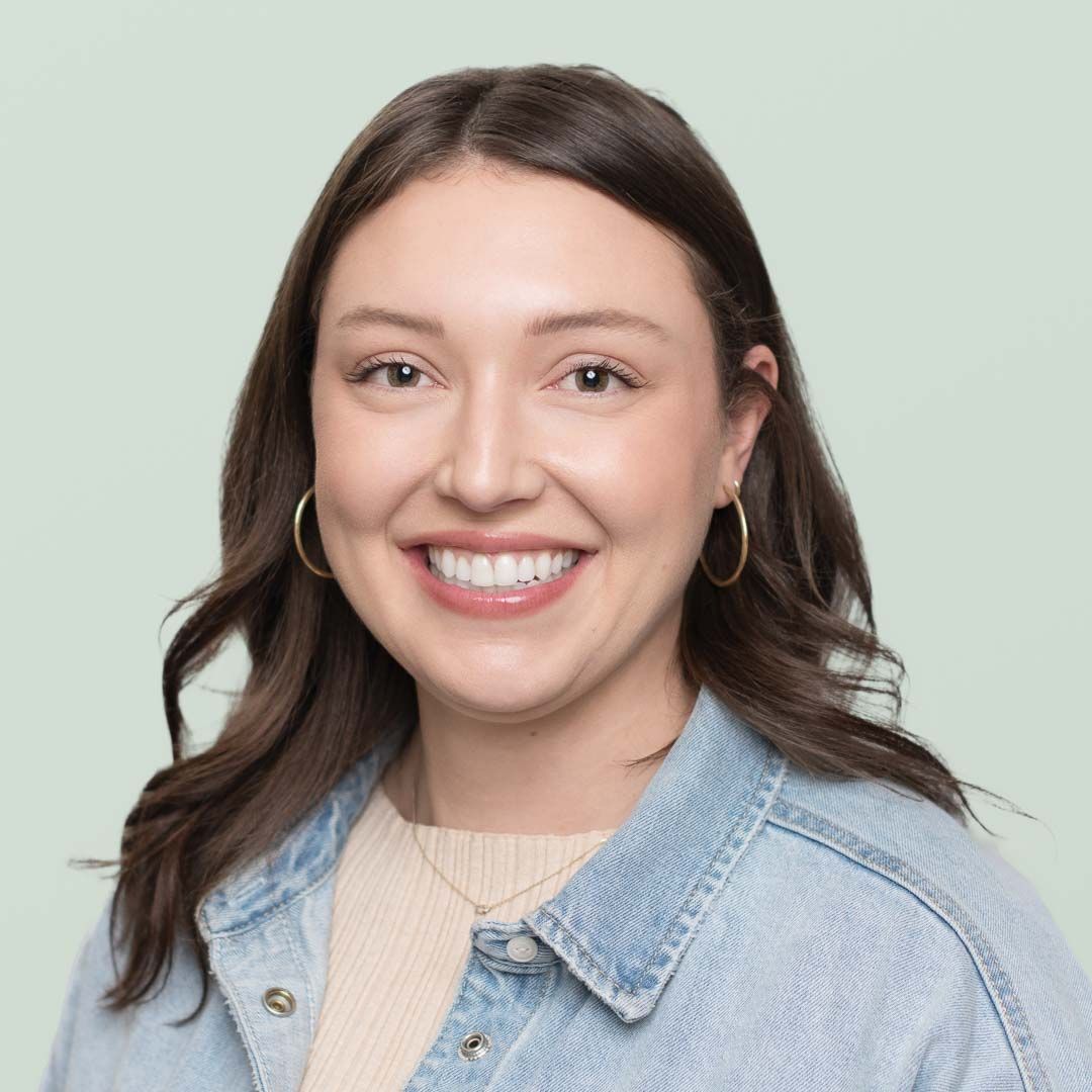 A woman is smiling in front of a wooden wall.