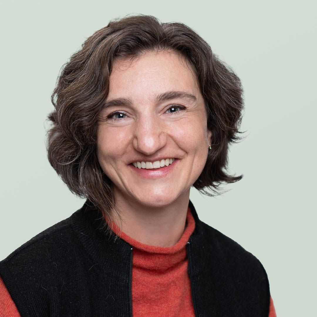 A woman wearing a blue jacket and earrings is smiling for the camera.