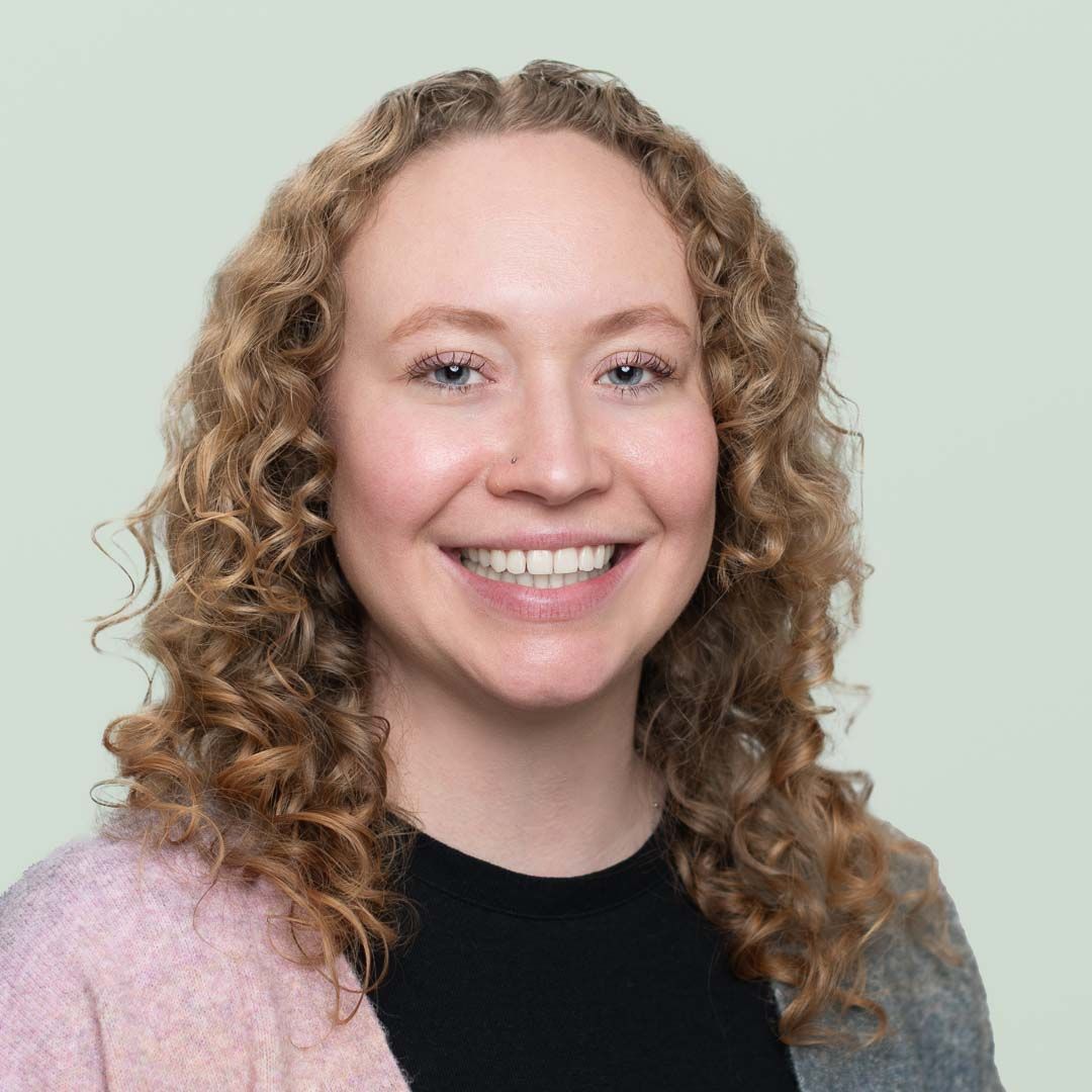 A woman with curly hair is smiling in front of a tree.