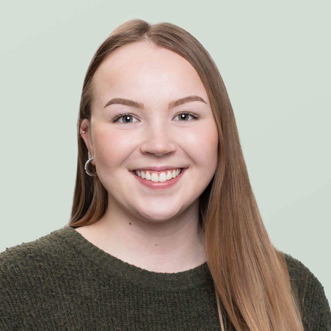 A woman in a black shirt is smiling in front of a bush with red leaves.