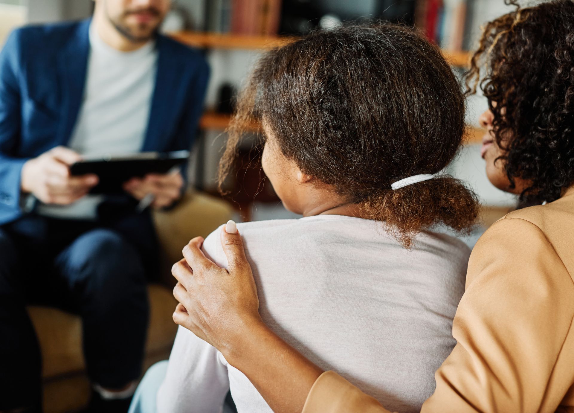 A mother and daughter are sitting on a couch talking to a female psychologist.