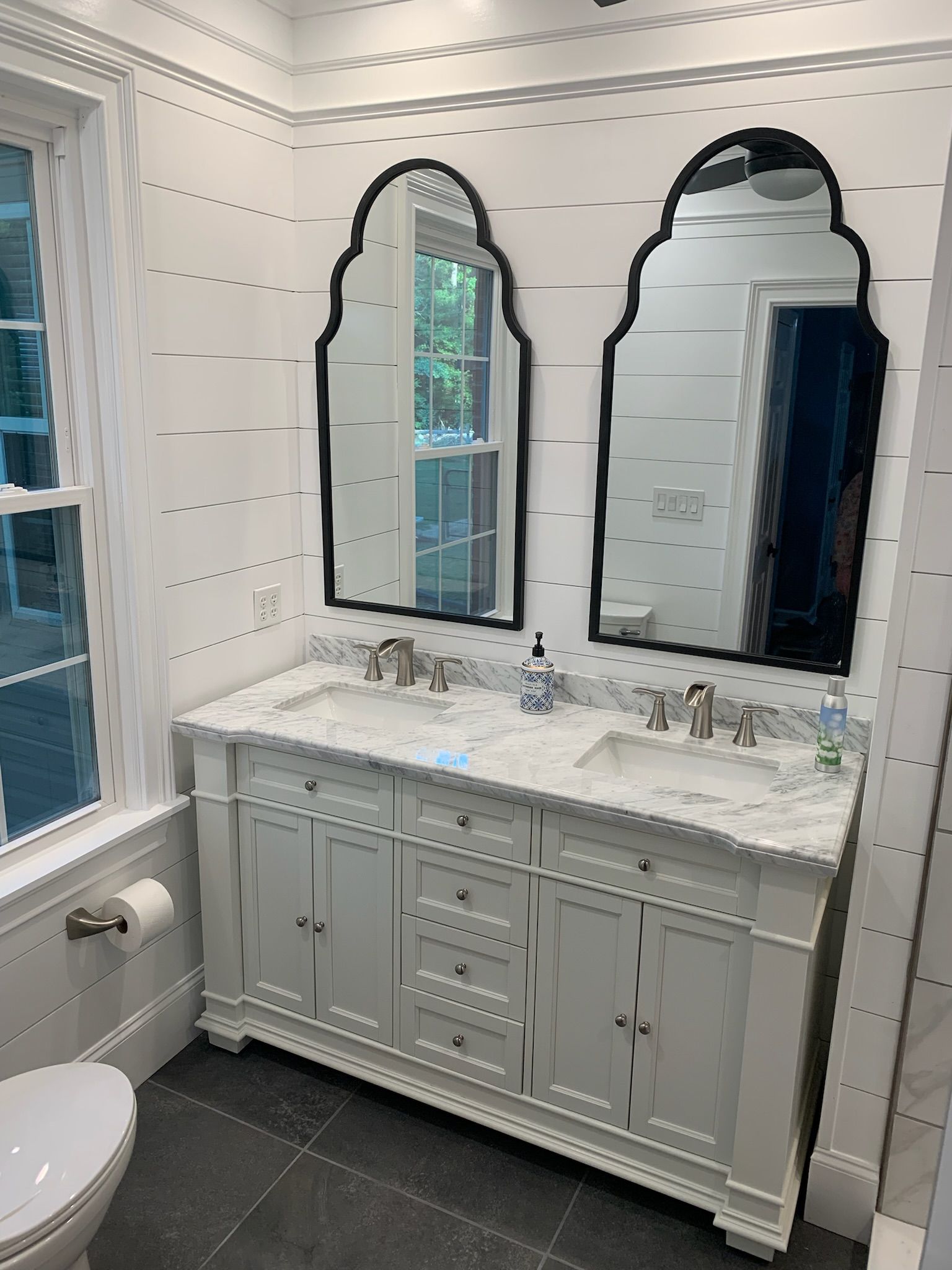 A bathroom with two sinks , two mirrors and a toilet.