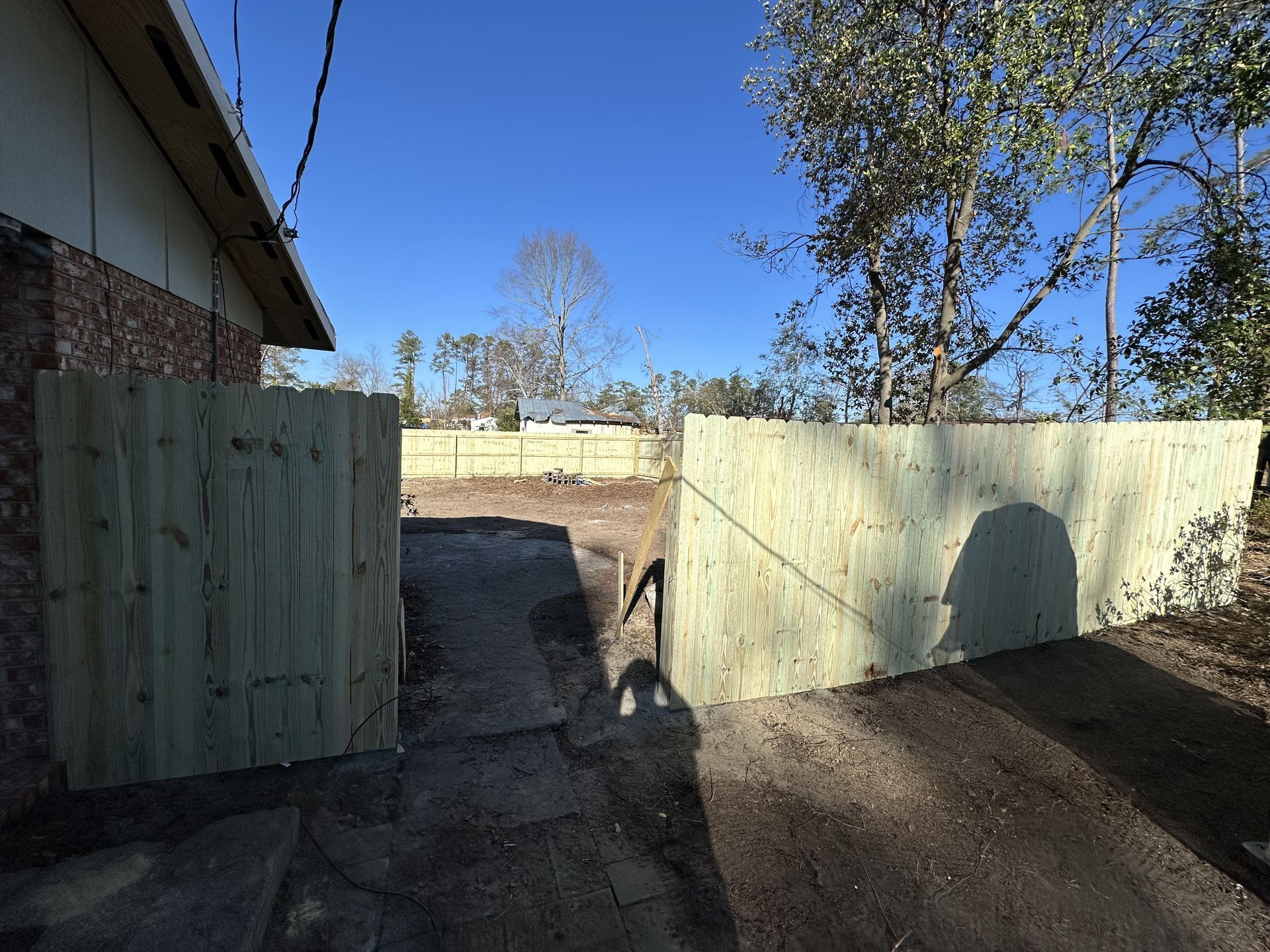 A wooden fence surrounds a dirt area in front of a house