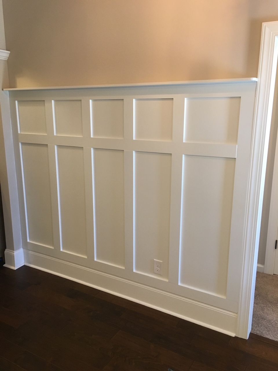 A wall with white paneling and a wooden floor in a living room.