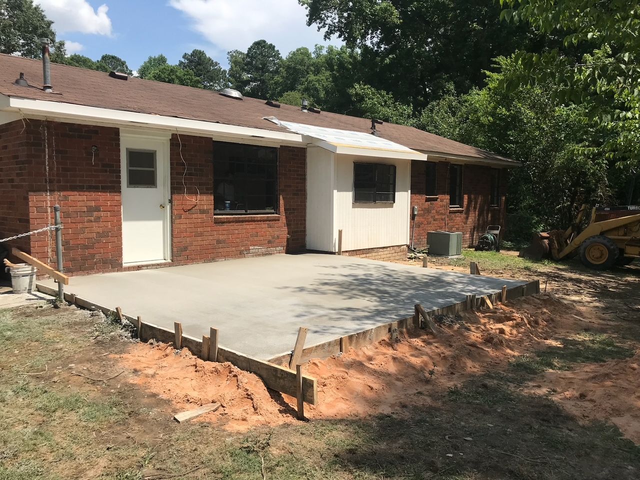 A brick house with a concrete driveway being built in front of it.