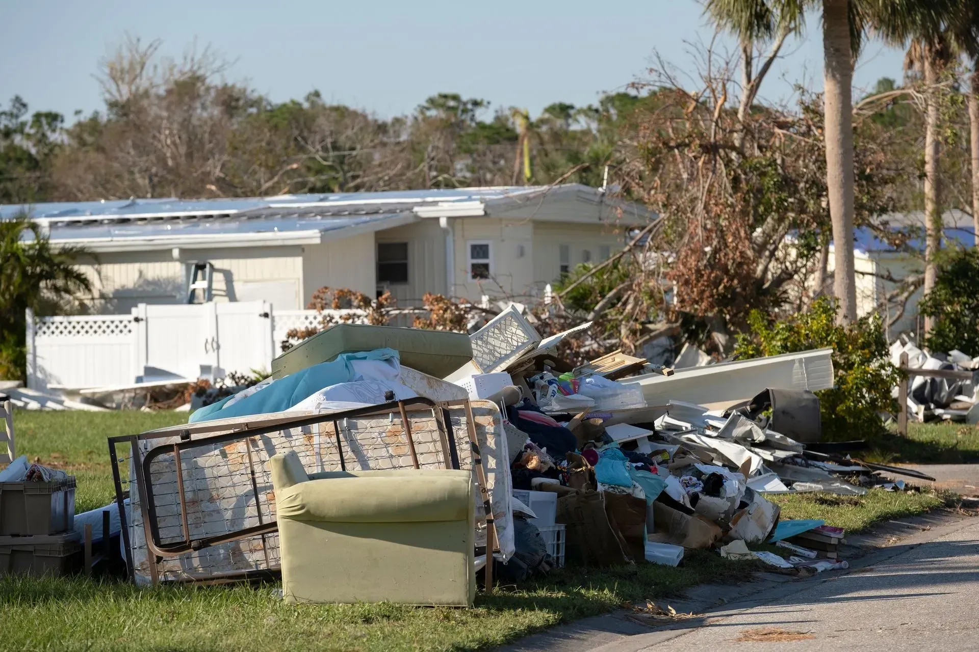 Pile of debris in front of a damaged house after a hurricane; broken furniture and household items on the lawn.