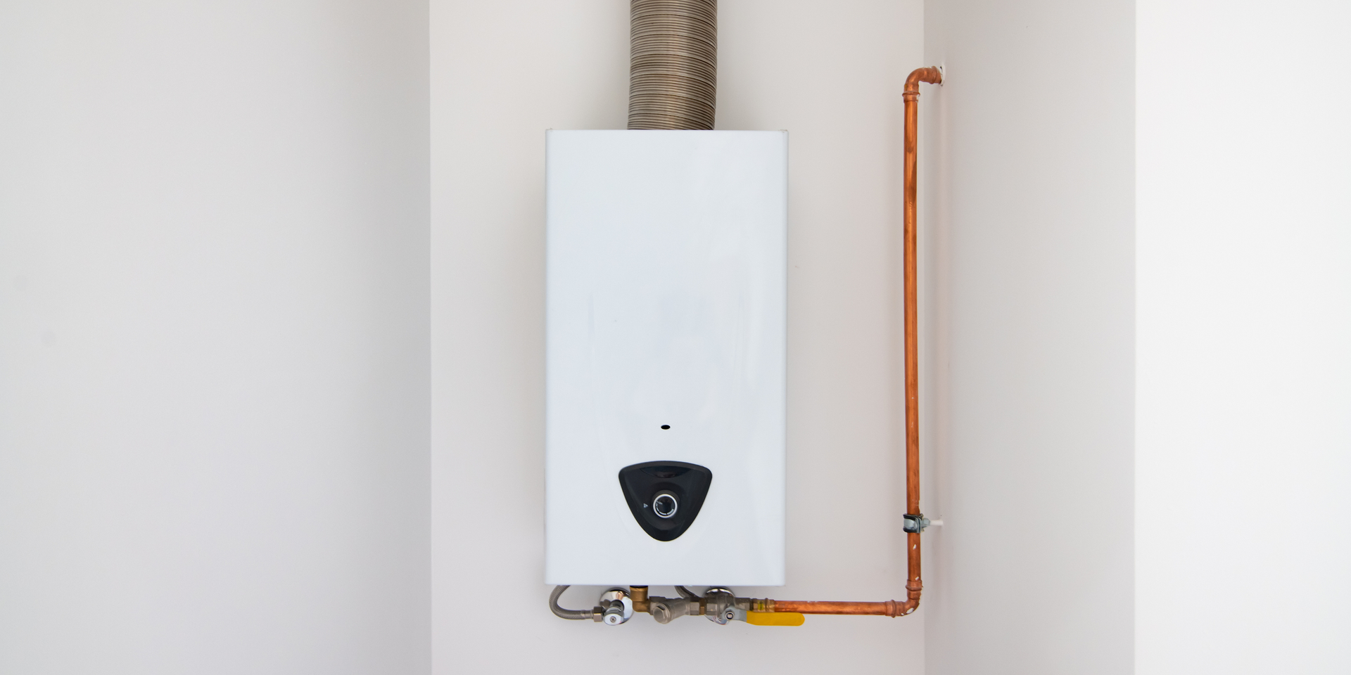 White gas boiler attached to a wall, with copper piping and exhaust vent.
