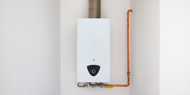 White wall-mounted gas boiler with copper pipes, a metal vent, and a control panel.