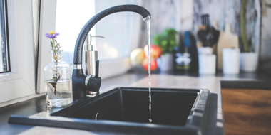 A kitchen sink with water running, a black faucet, and a vase of flowers on the counter.