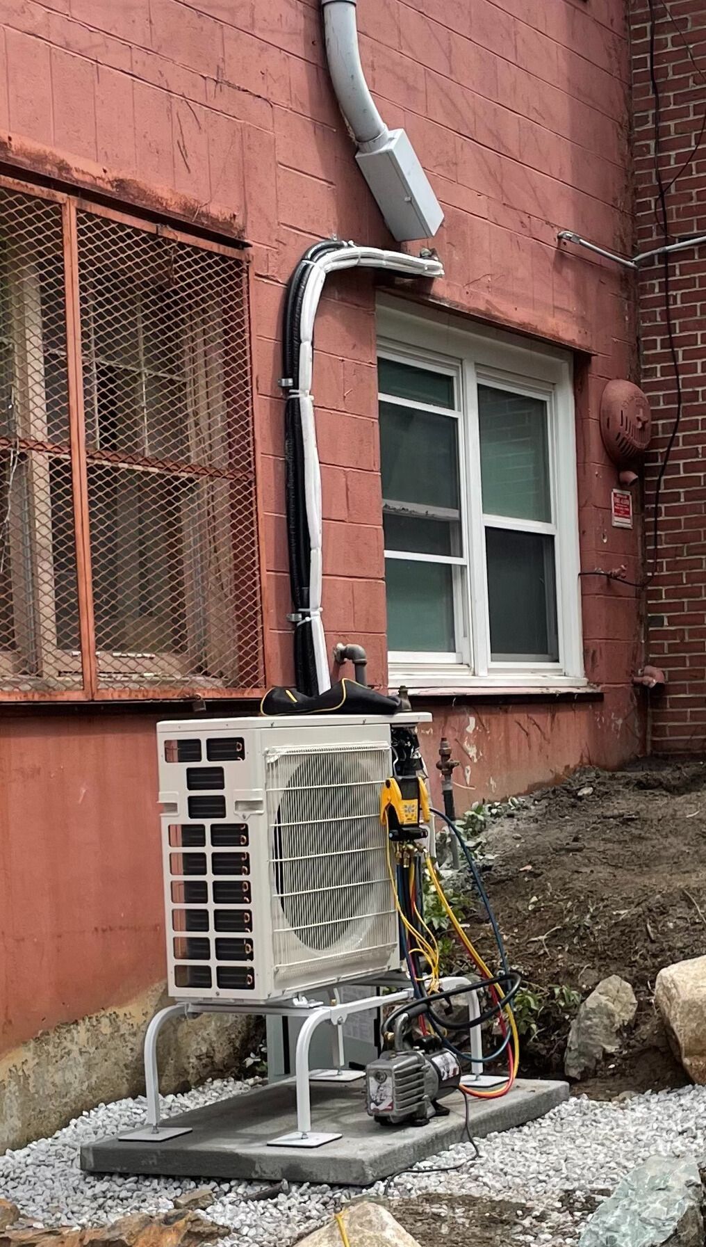 An air conditioner is being installed on the side of a brick building.