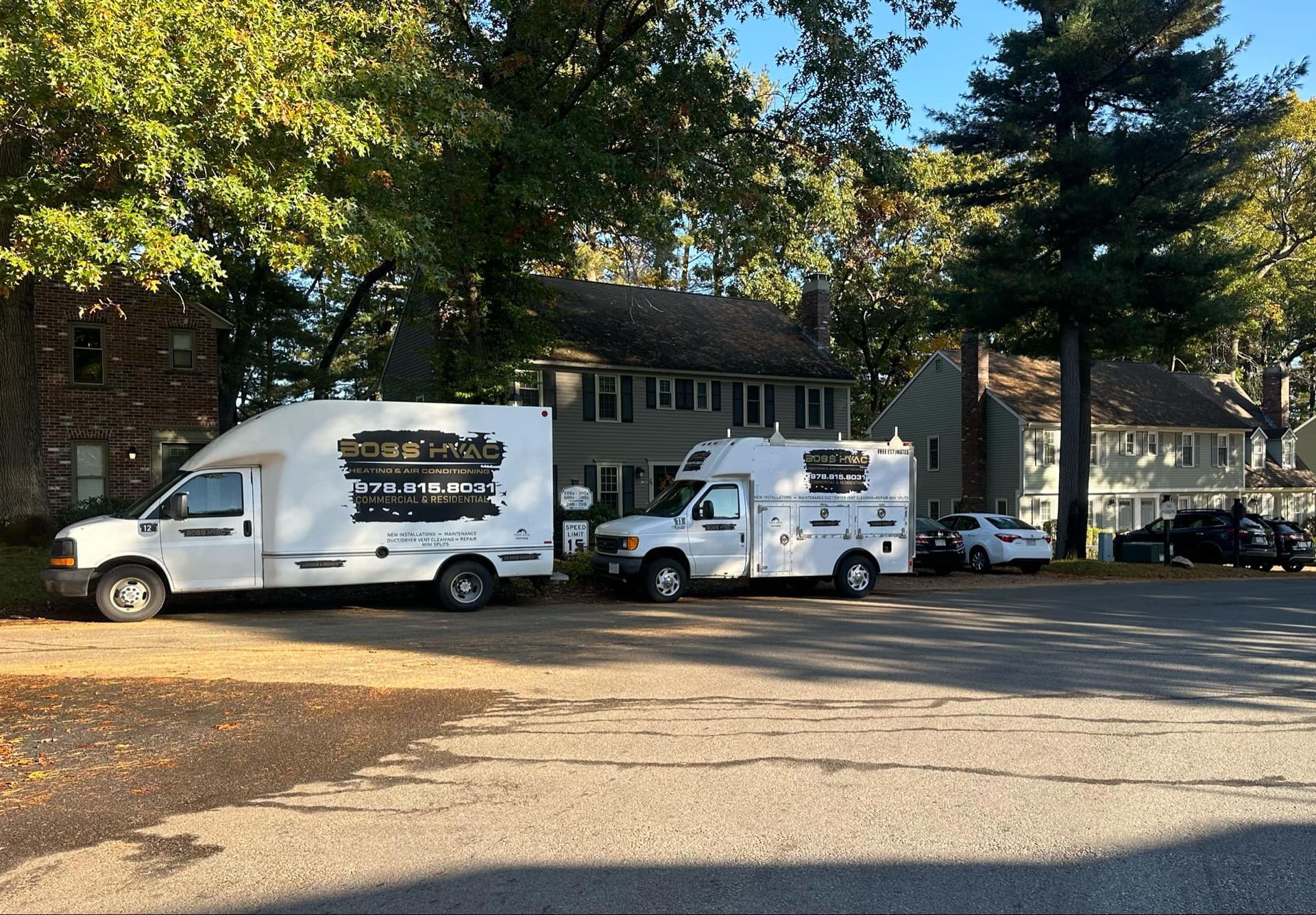 Two white vans are parked in a parking lot in front of a house.