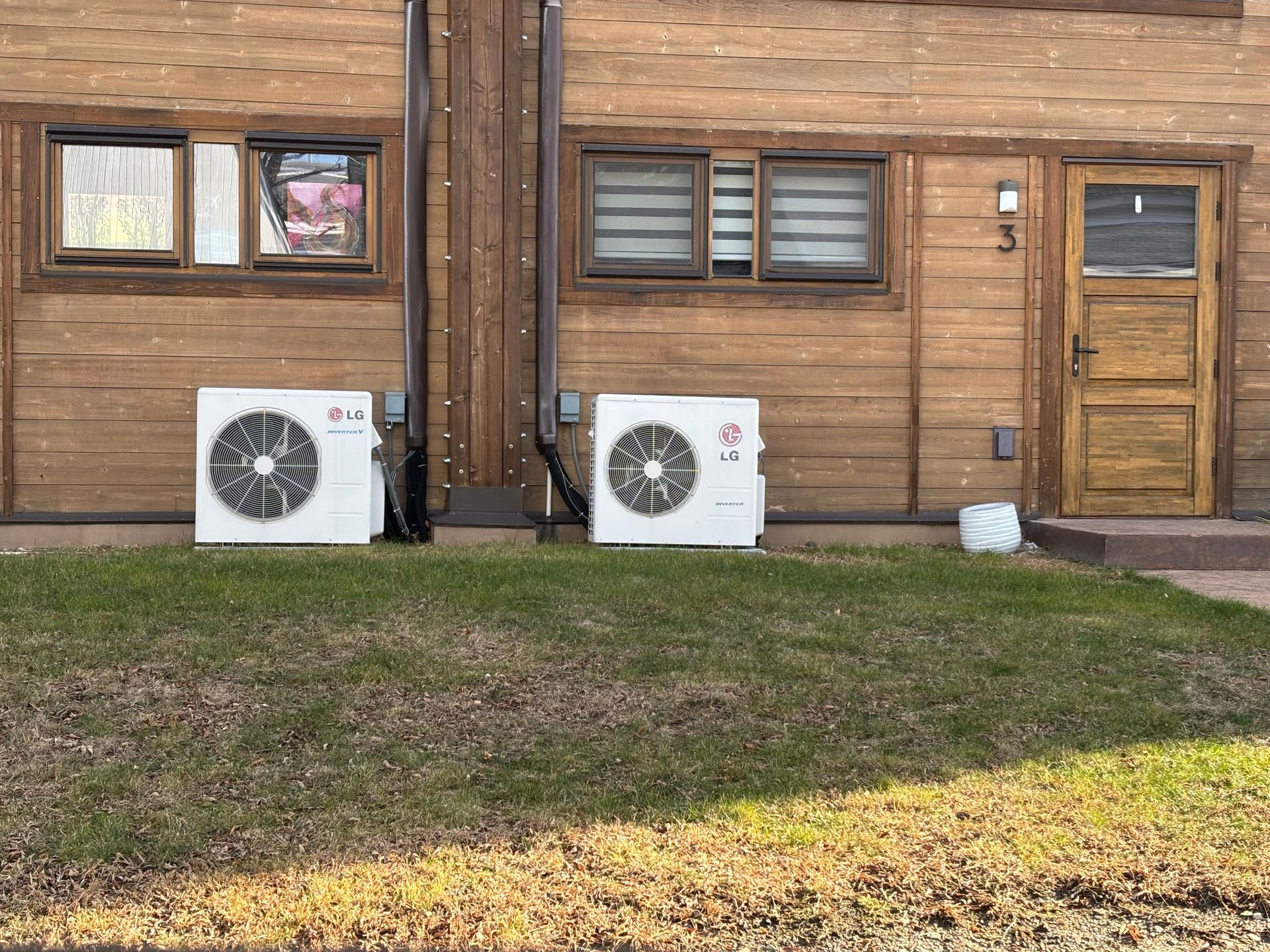 Two lg air conditioners are sitting outside of a wooden building.