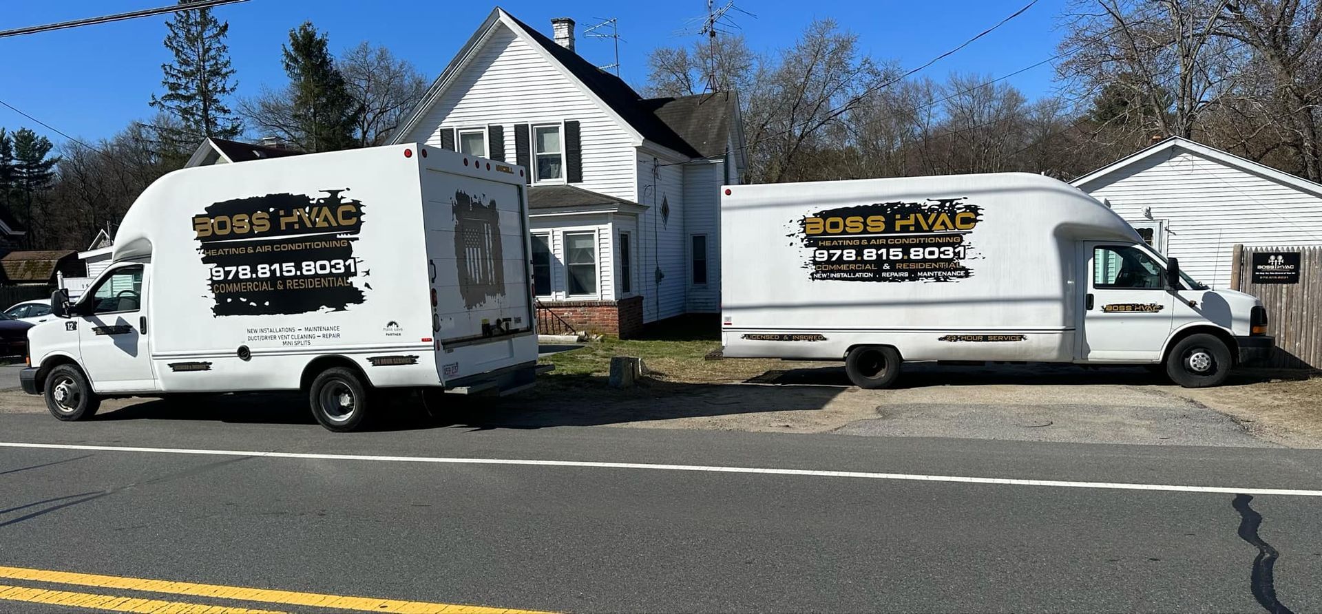 Two white trucks are parked on the side of the road in front of a house.