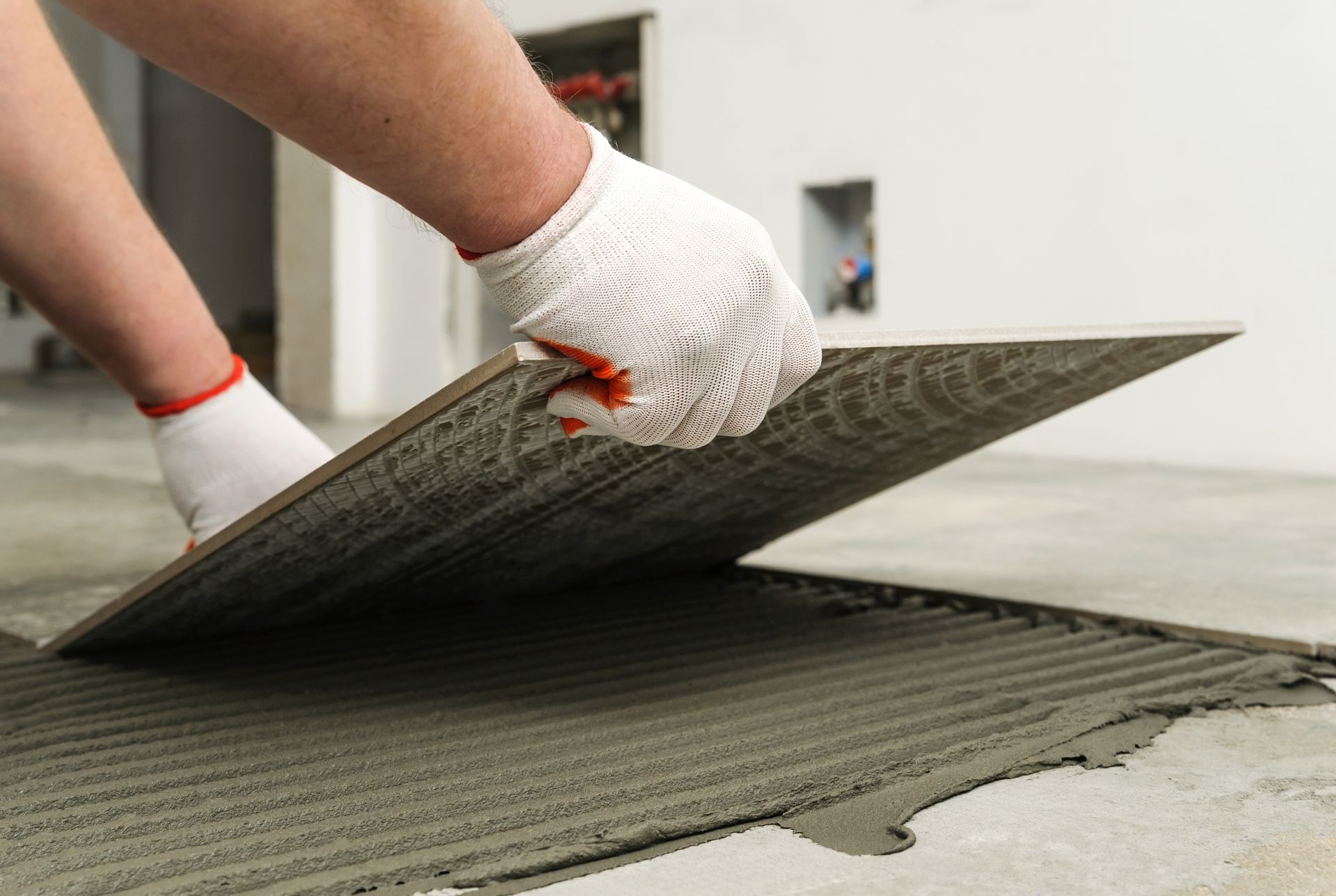Person wearing gloves placing a tile on a bed of mortar on the floor.