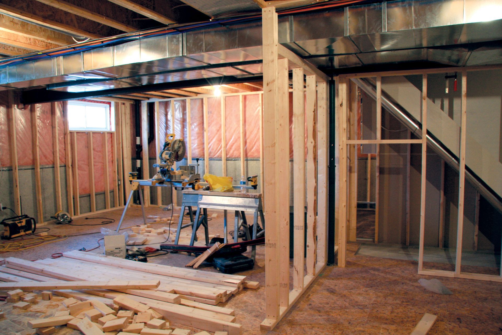 Basement under construction, with wooden studs, insulation, and tools.
